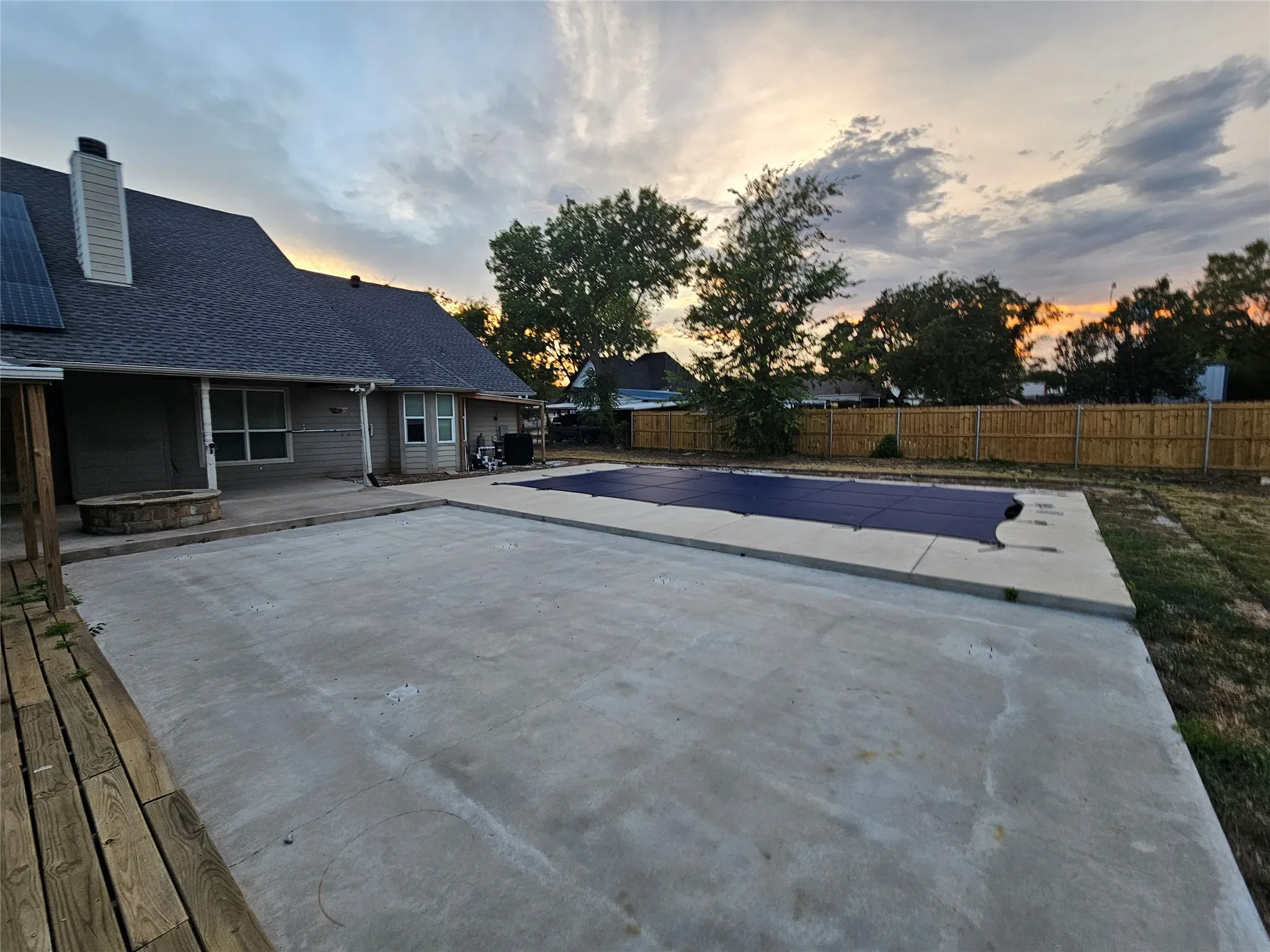 Concrete patio with an adjacent pool, wood deck, and a built-in fire pit