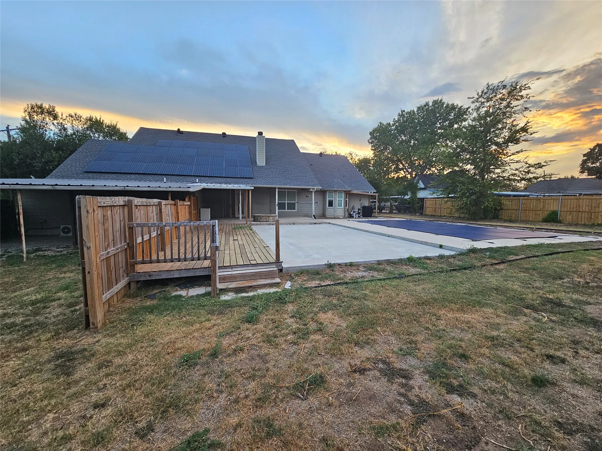 Rear exterior with solar panels, covered patio, wood deck, and an in-ground pool with a concrete surround