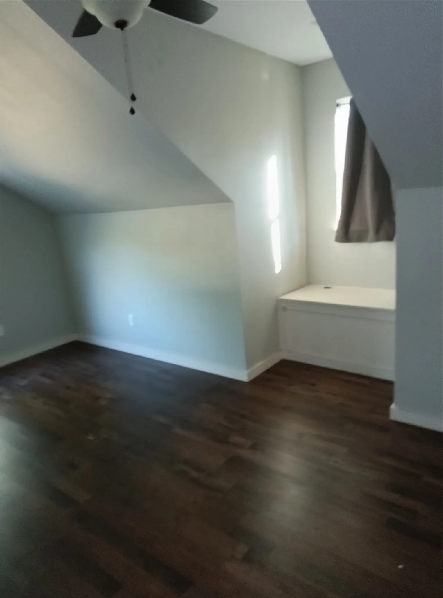 Sloped ceilings, wood-finish flooring, built-in window bench, and a ceiling fan