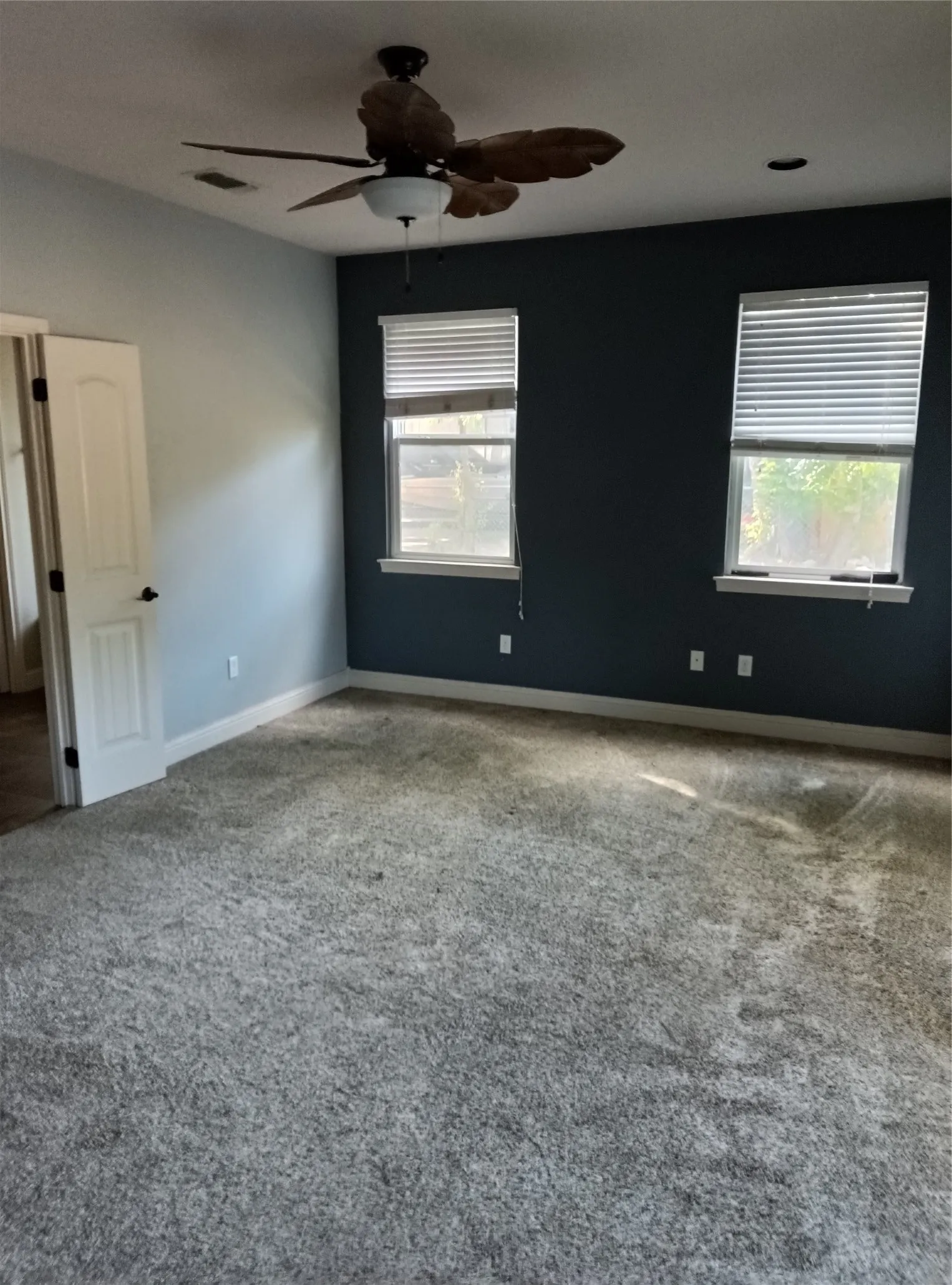 Spacious room featuring gray wall-to-wall carpeting, a dark accent wall, and two windows with blinds