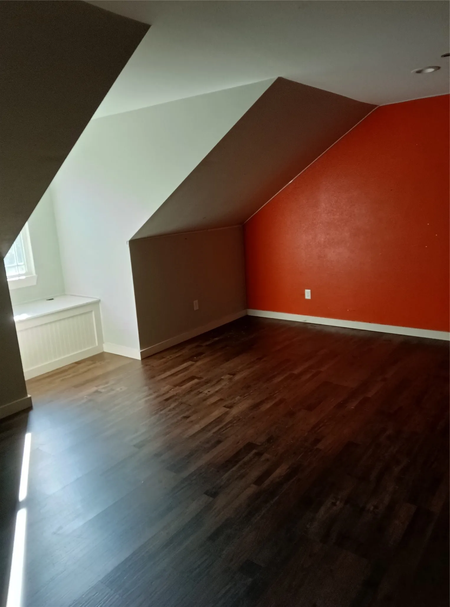 Dark wood-finish flooring, built-in window bench with beadboard detail, sloped ceilings, and accent wall