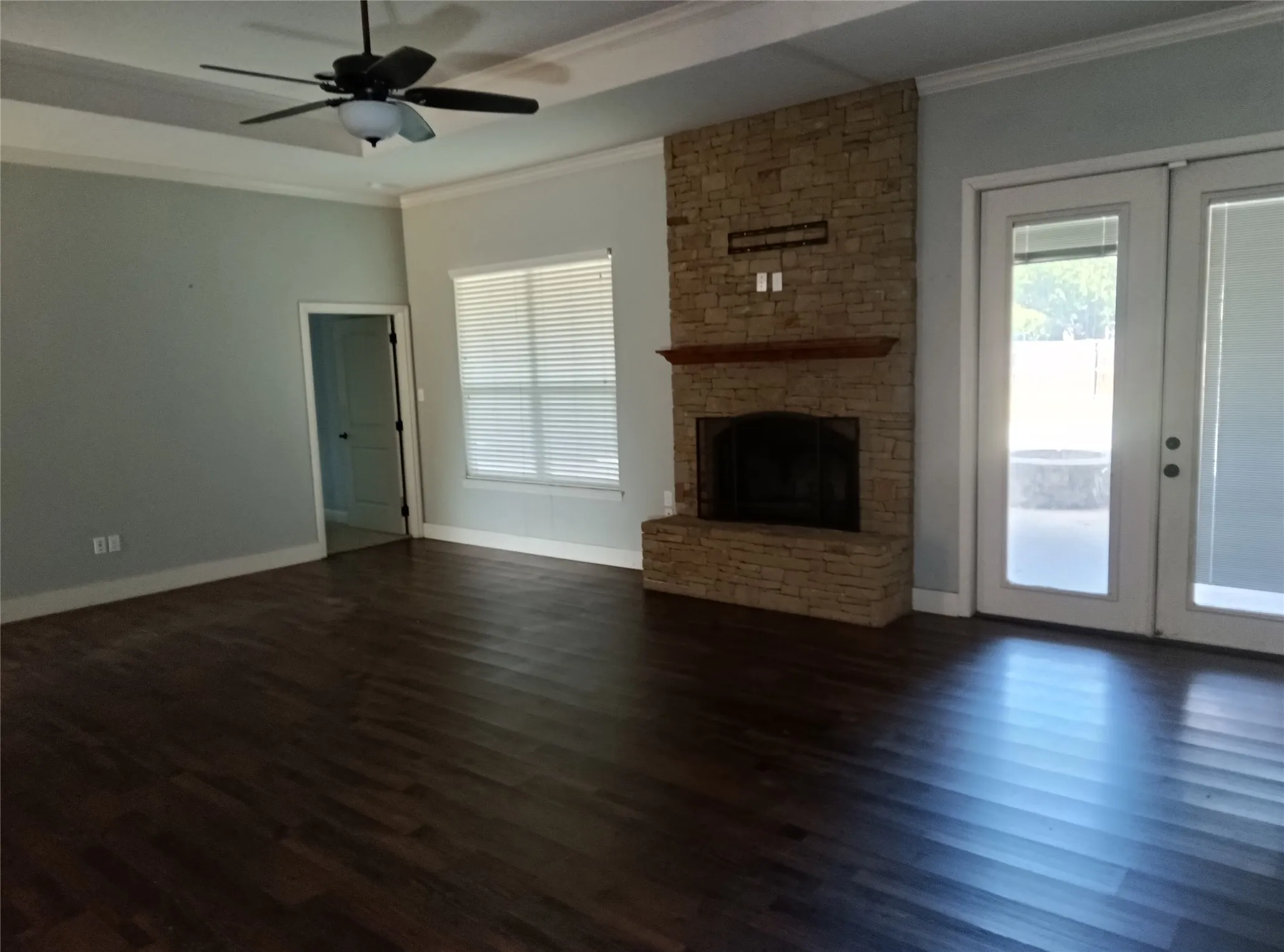 Stacked stone fireplace with a wood mantel, wood-finish flooring, and a ceiling fan