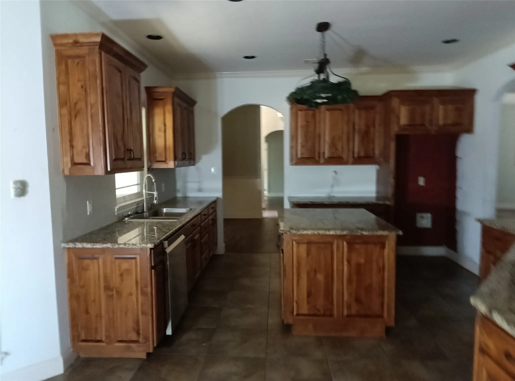 Kitchen featuring wood cabinetry, granite countertops, tile flooring, a double basin sink, and an arched doorway
