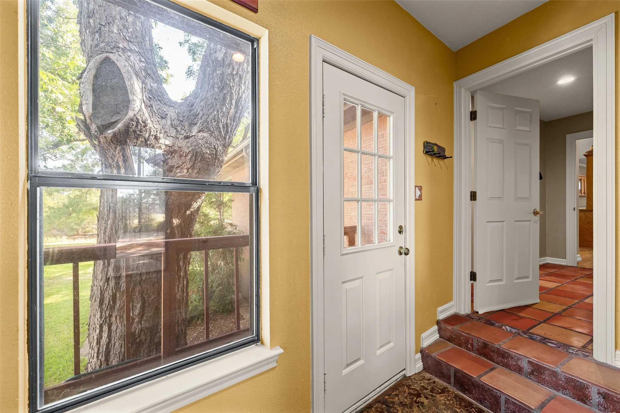Entryway featuring a paneled door with divided lites, terracotta-style floor tiling, and a large window overlooking exterior wood railing