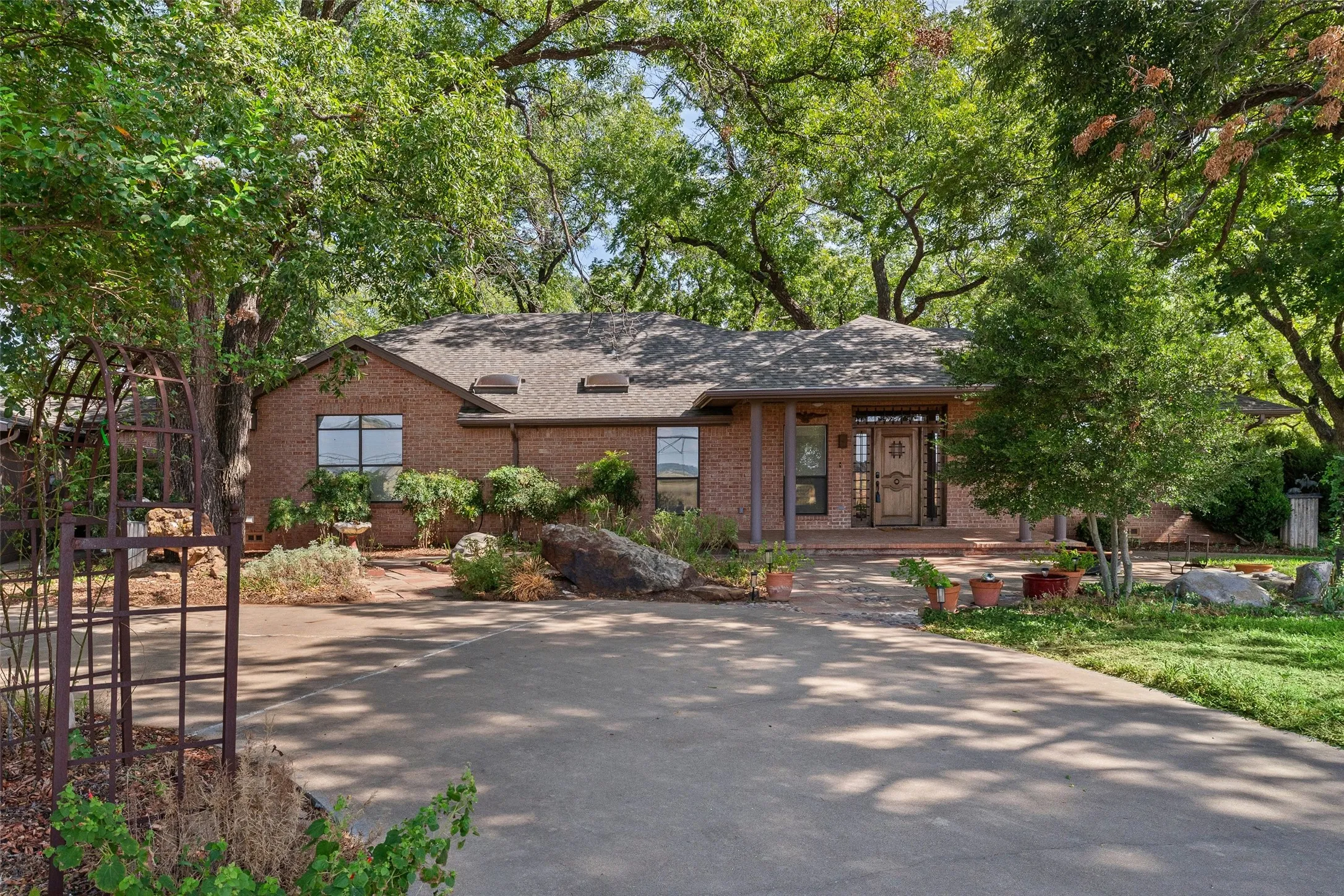 Brick exterior with a gabled roofline, covered front porch, and mature trees providing ample shade