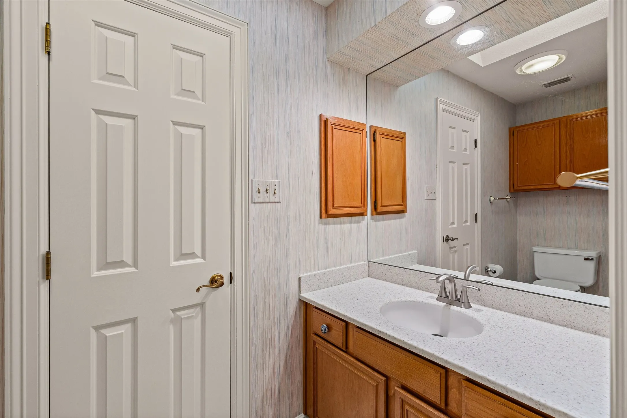 Recessed lighting illuminating a vanity with a white countertop, an undermount sink, and a chrome faucet
