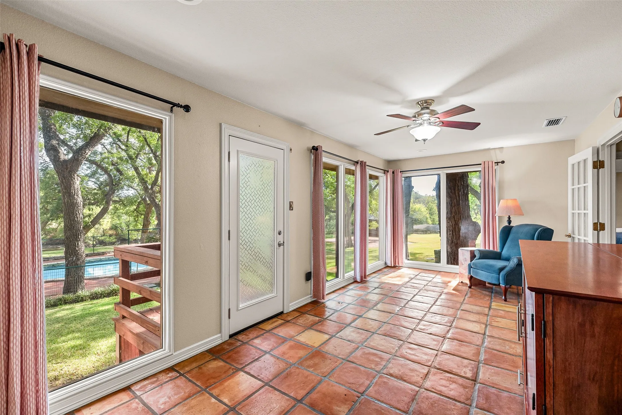 Terracotta tile flooring, multiple picture windows, a ceiling fan, and French doors