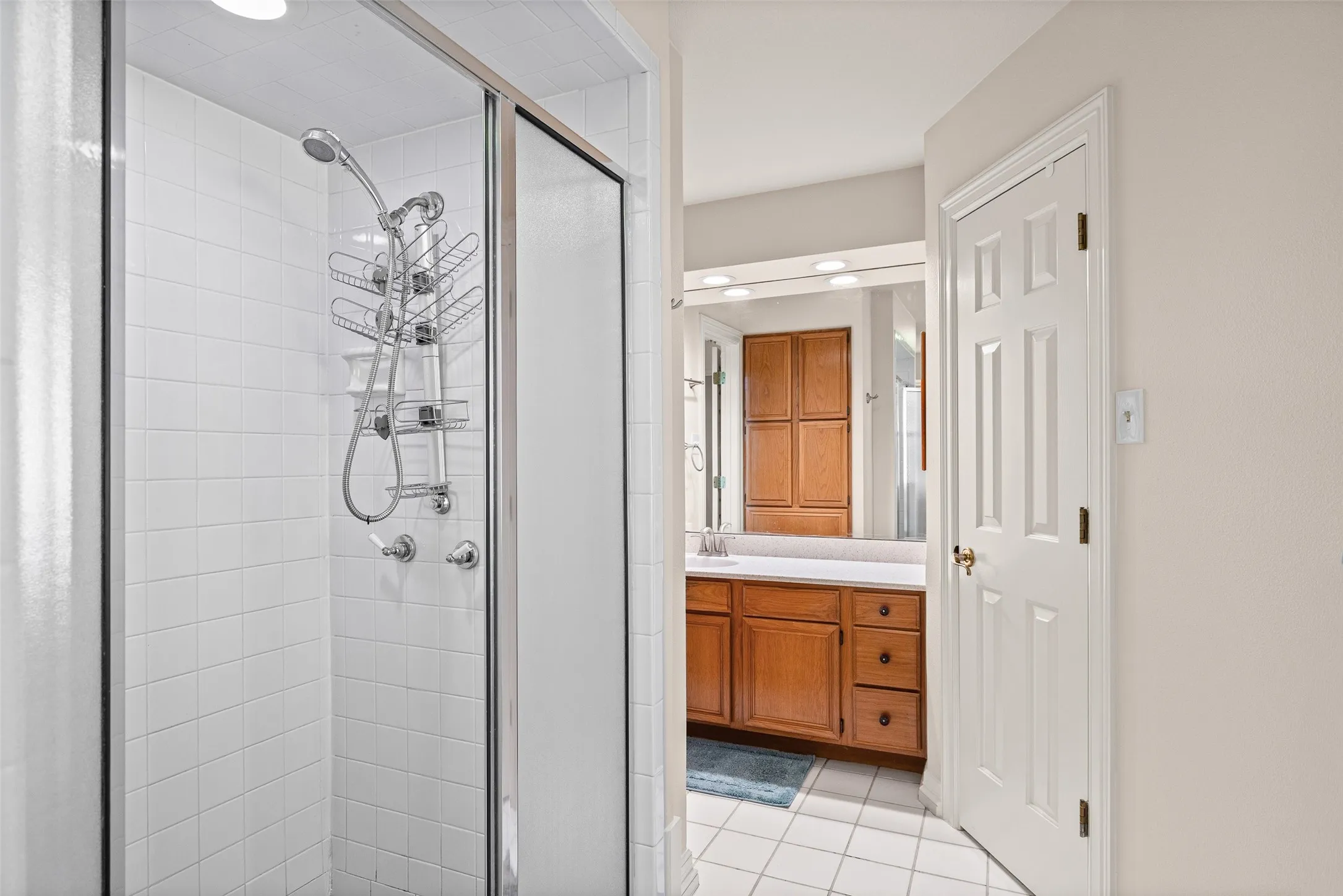 Glass-enclosed shower with white tiled walls and a handheld shower head