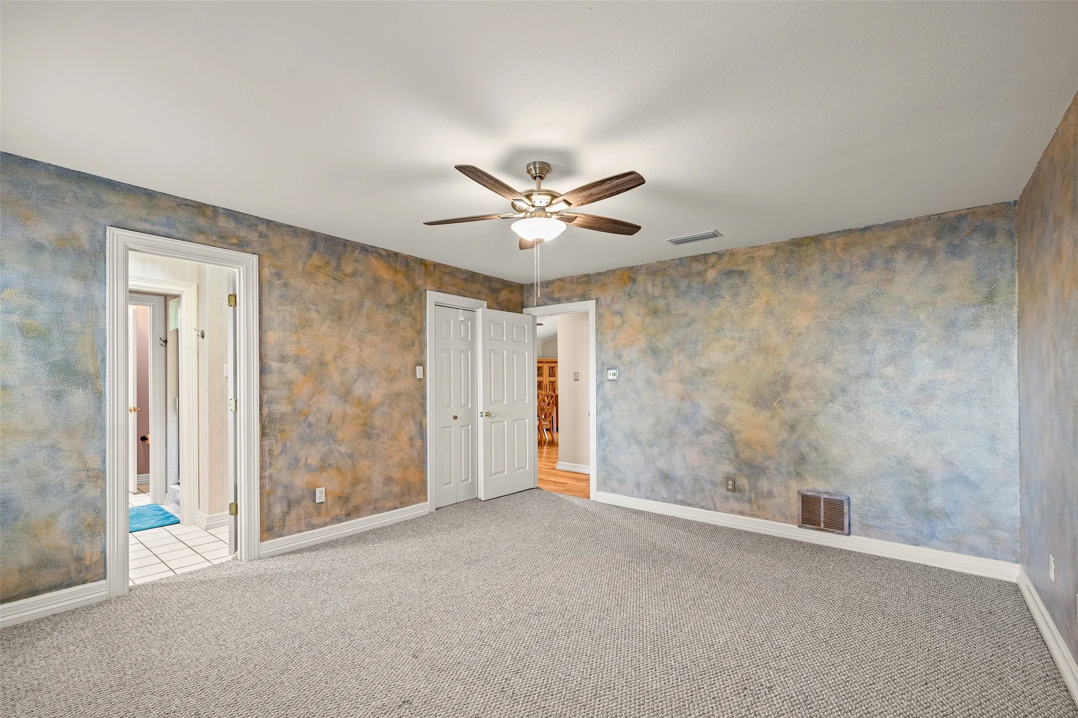 Textured wall finish, ceiling fan with integrated lighting, carpeted flooring, white trim, and white paneled doors