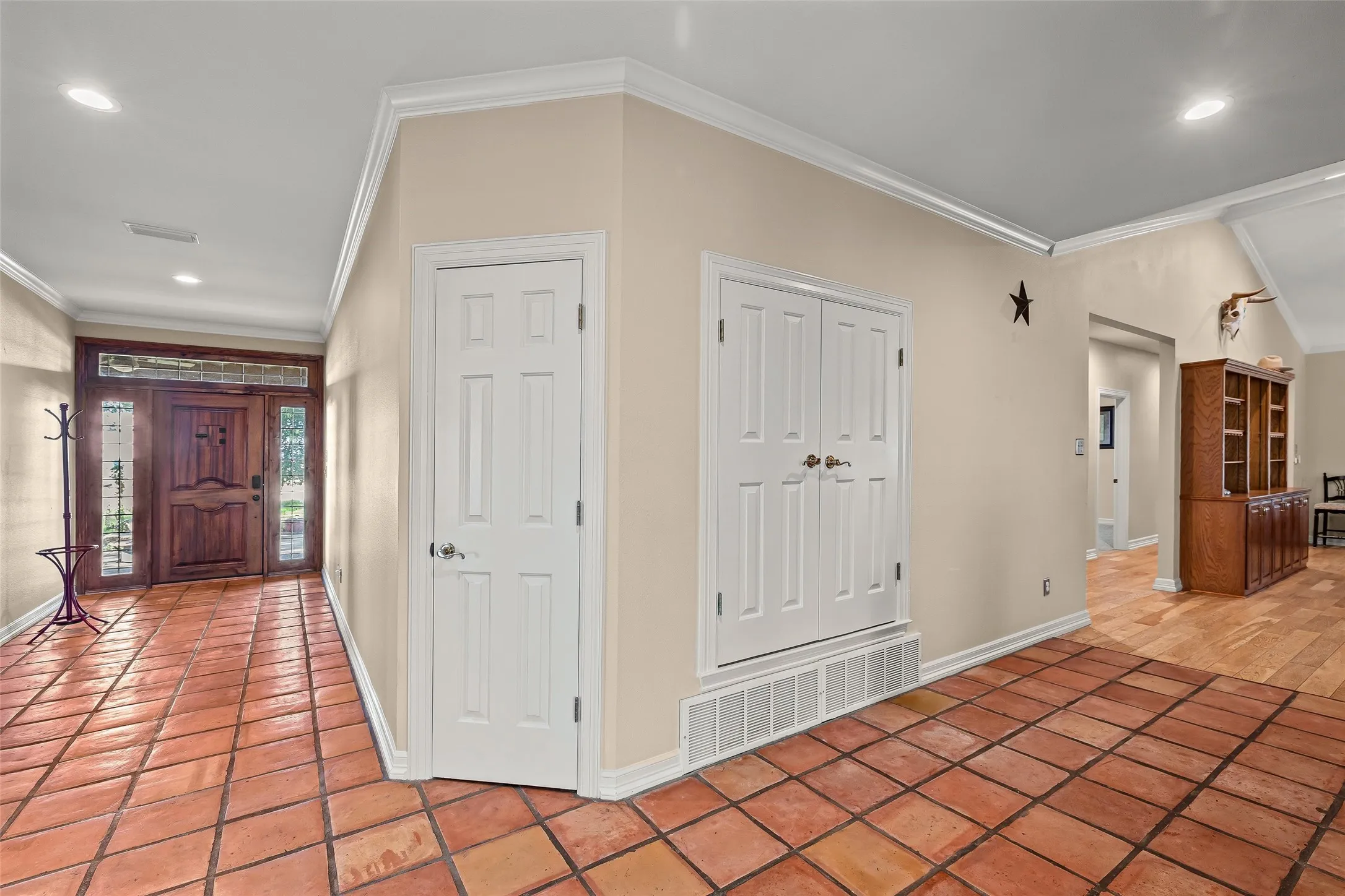 Entryway featuring terra cotta tile flooring, crown molding, and a wood entry door with sidelights