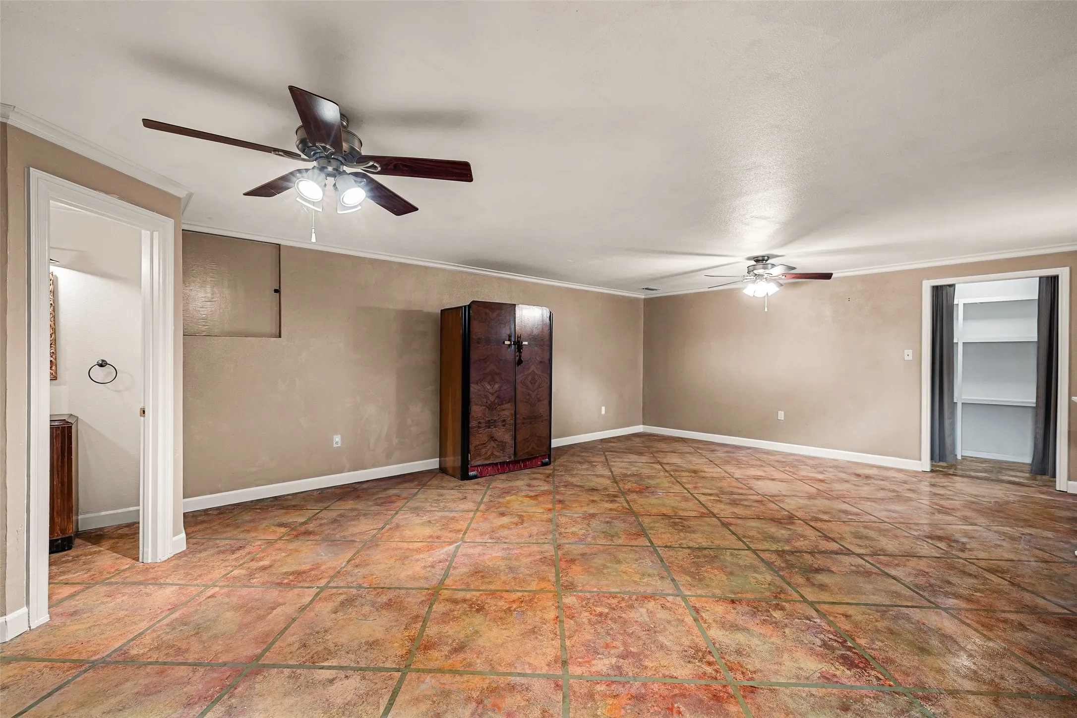Spacious room featuring tile flooring, crown molding, and two ceiling fans with integrated lighting