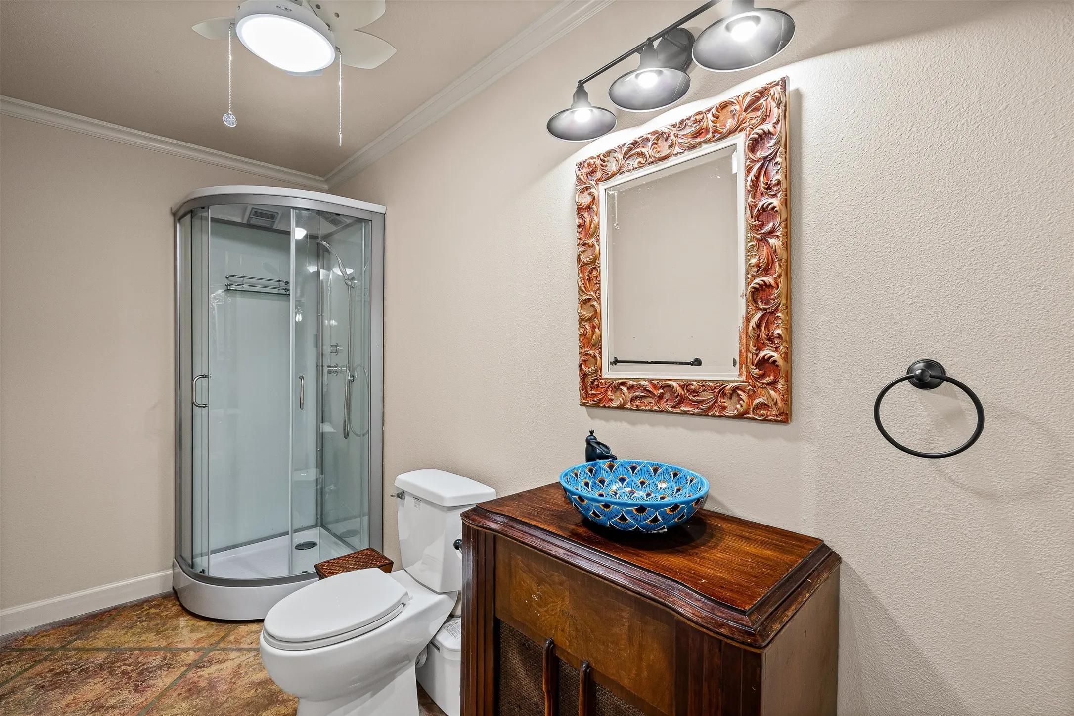 Corner glass shower enclosure, white ceiling fan, vanity with wood-finish cabinet, and framed mirror with track lighting