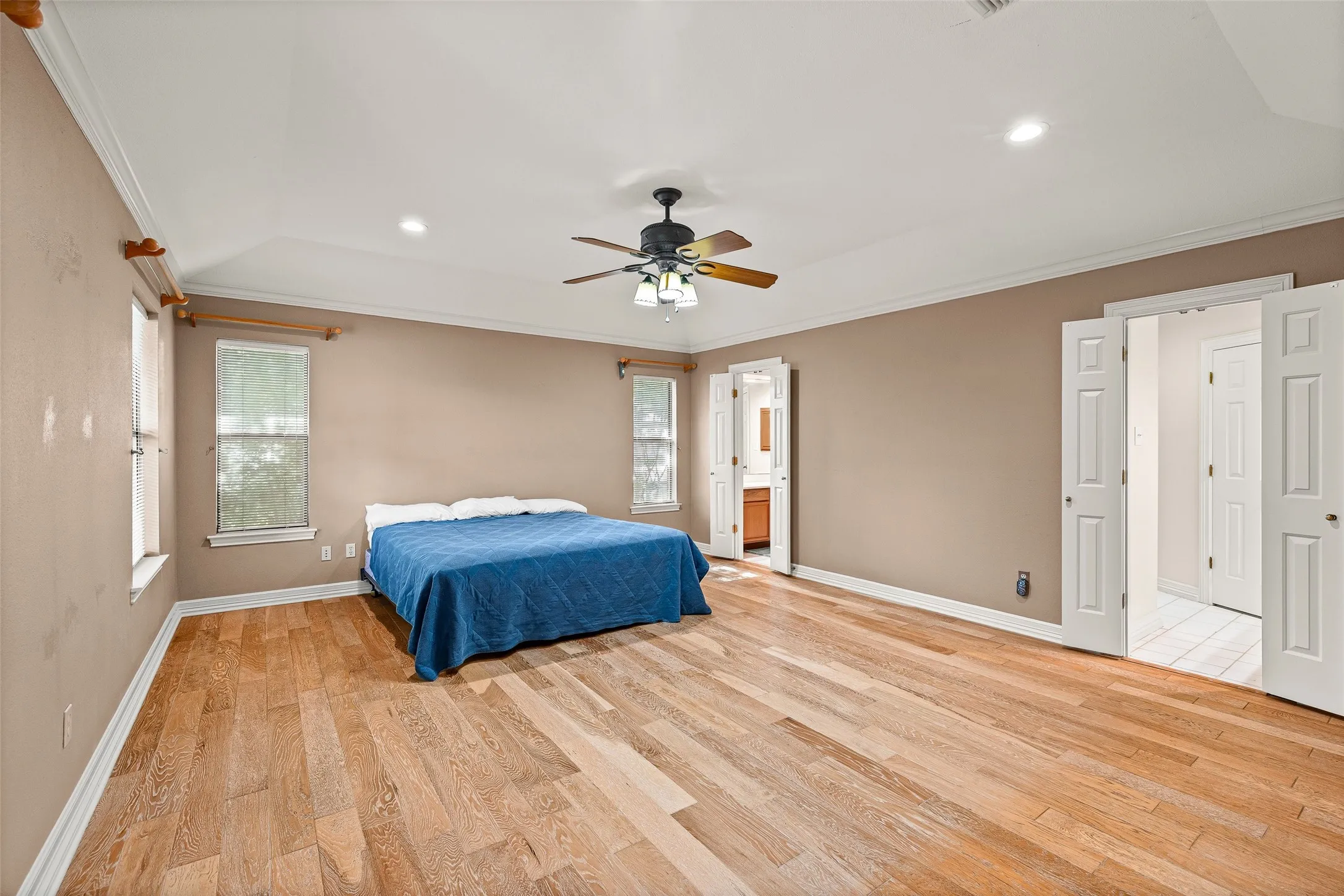 Spacious room featuring wood-finish flooring, a tray ceiling, and a ceiling fan with integrated lighting