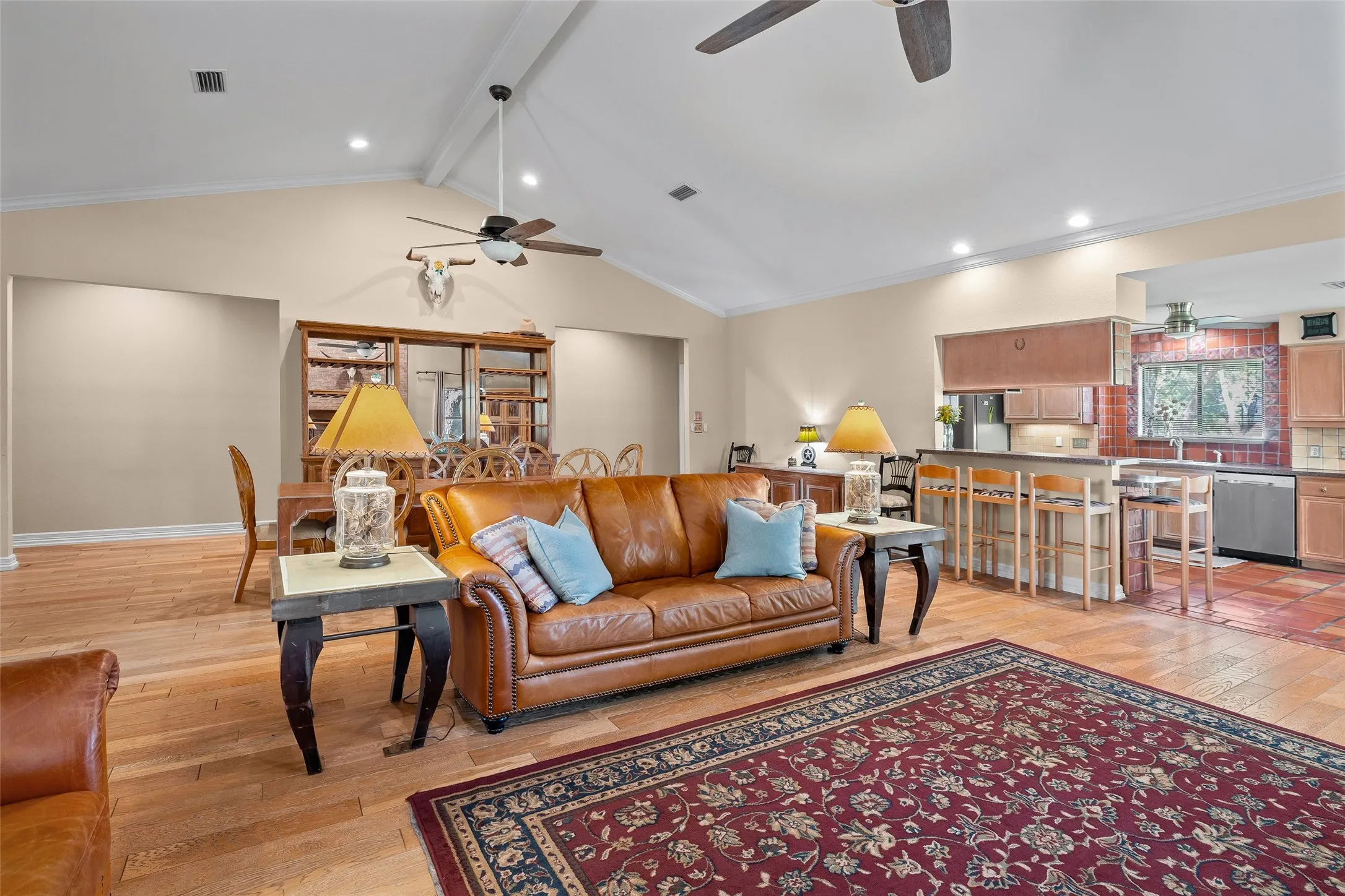 Vaulted ceilings with recessed lighting, wood-finish flooring, kitchen with bar seating, integrated stainless steel appliances, and terra cotta tile flooring
