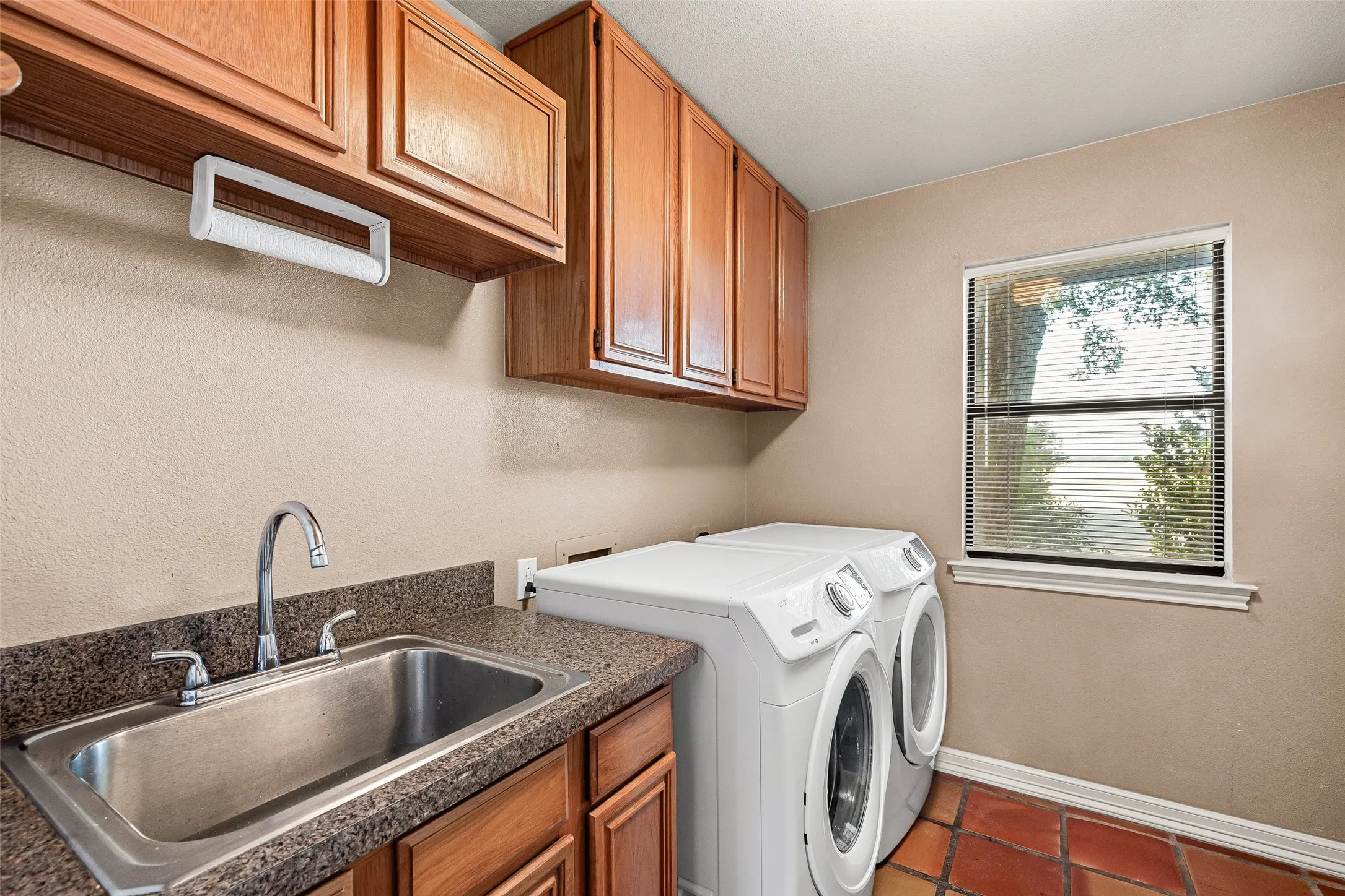 Utility room with upper cabinetry, a stainless steel sink, a window, and terracotta-style flooring