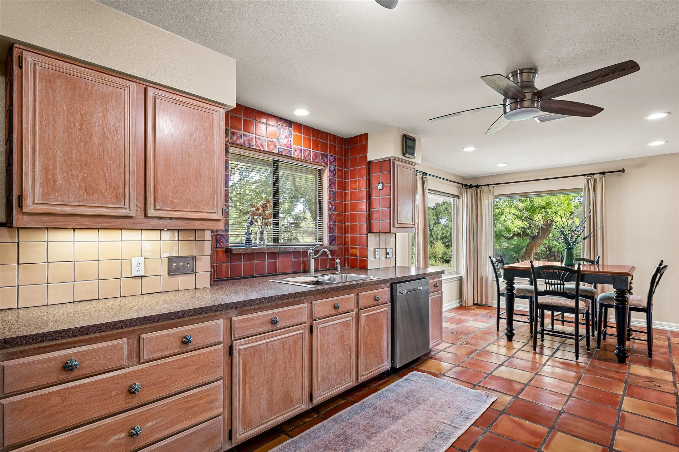 Kitchen featuring wood cabinetry, integrated stainless steel dishwasher, tile backsplash, and a ceiling fan with integrated lighting