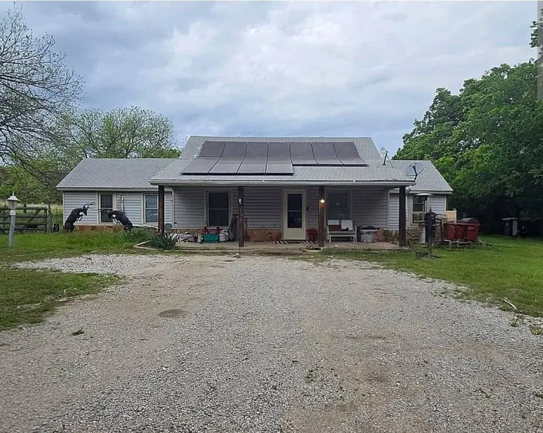 Gable roof with integrated solar panels, covered front porch, horizontal siding, stone accent base, and gravel driveway