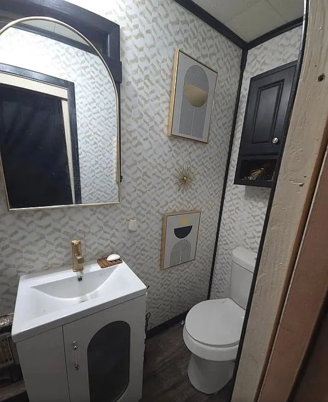 Vanity with integrated sink, gold-finish faucet, wall-mounted mirror, and patterned wallpaper