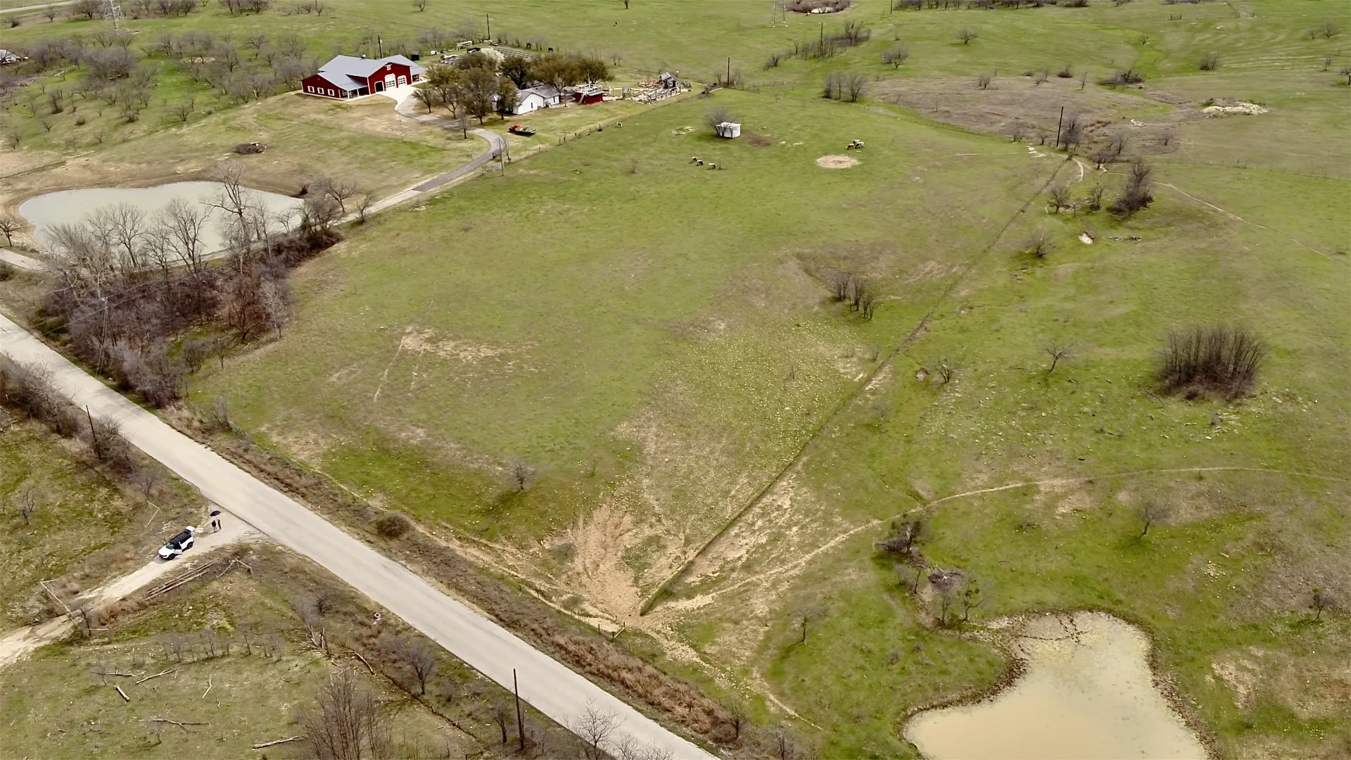 Paved road frontage, two visible ponds, expansive green acreage, and a distant residential structure