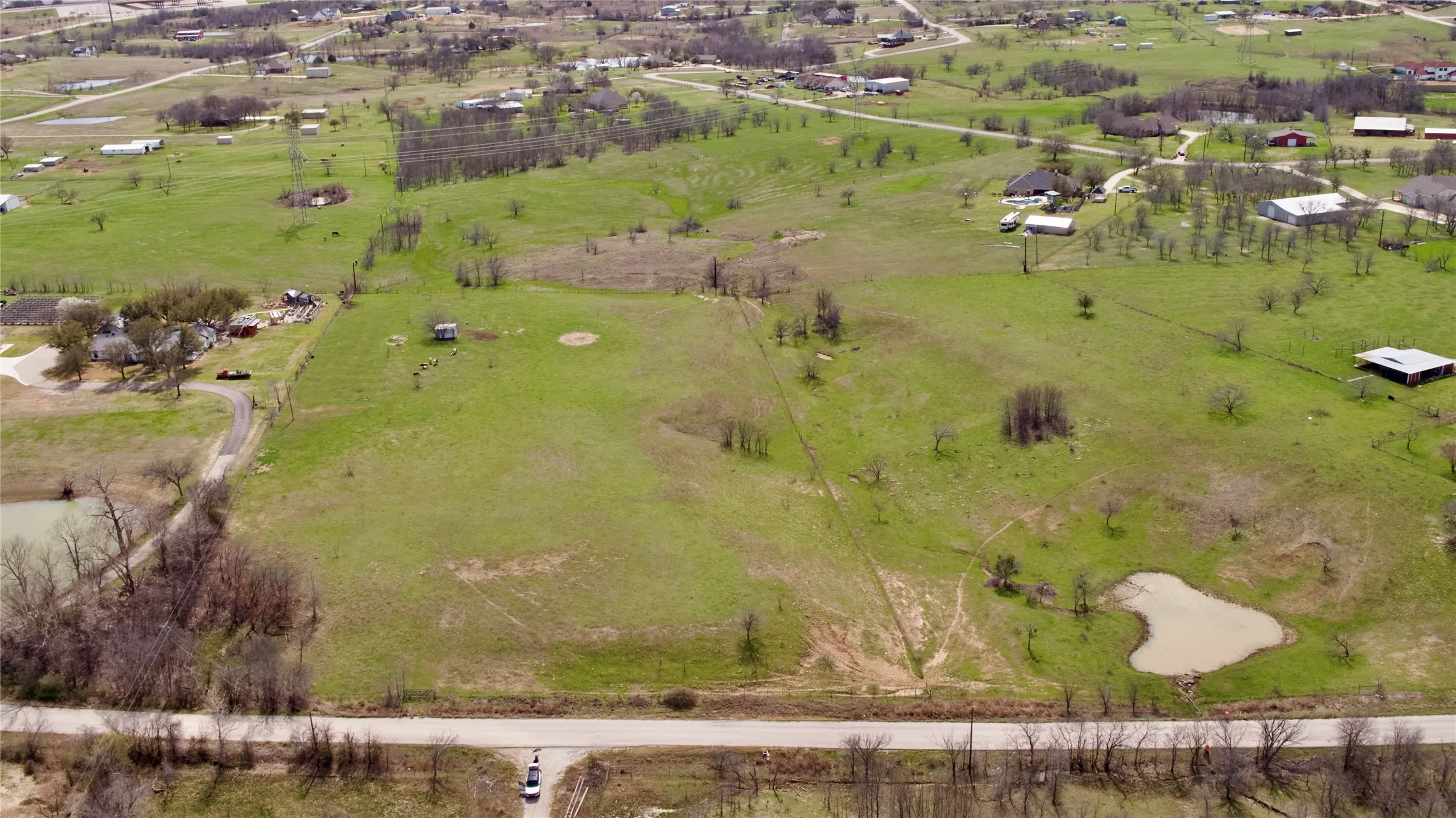Expansive green acreage featuring a visible roadway, natural ponds, and scattered trees