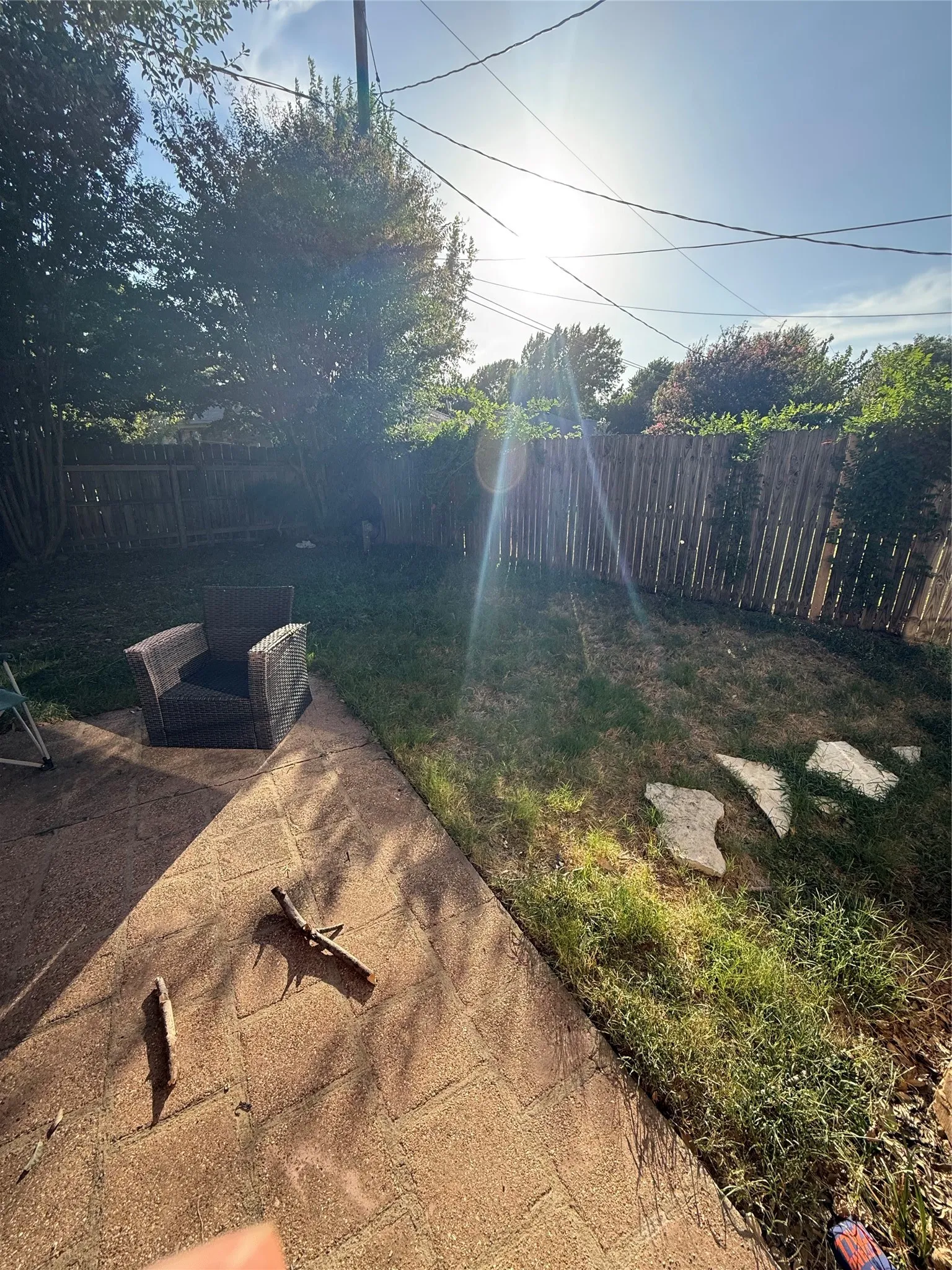 Paved patio with a grass area, mature perimeter trees, and wood fencing