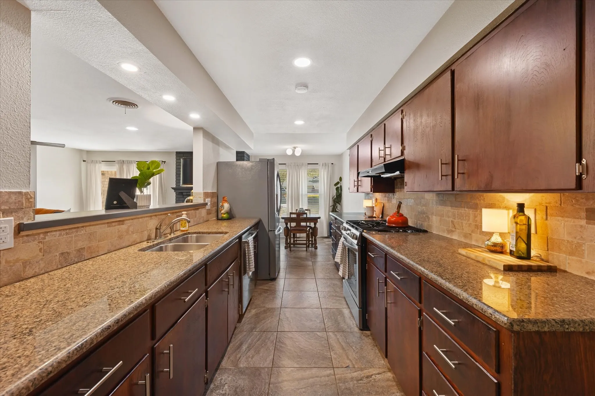 Galley kitchen featuring wood-finish cabinetry, stone countertops, a tile backsplash, and stainless steel appliances