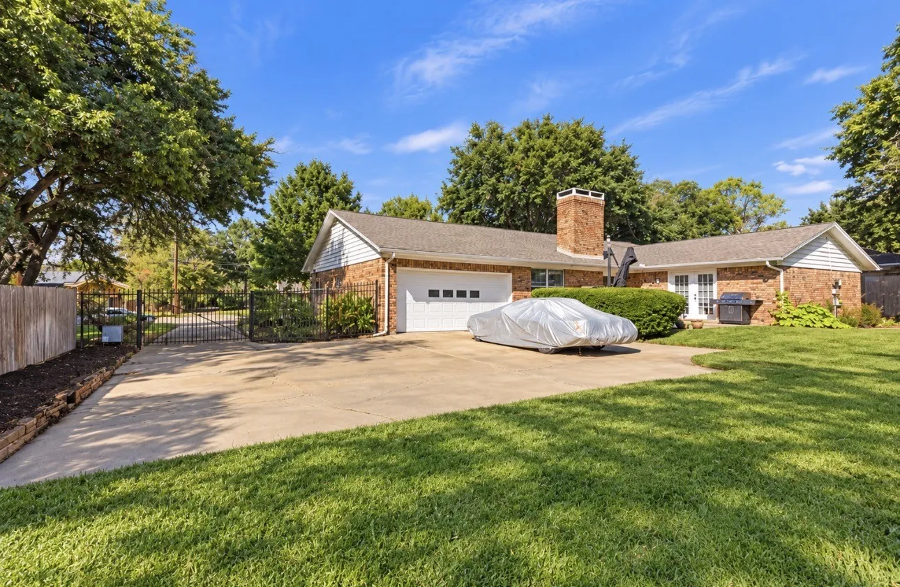 Brick and siding exterior with a two-car garage, mature trees, and a concrete driveway
