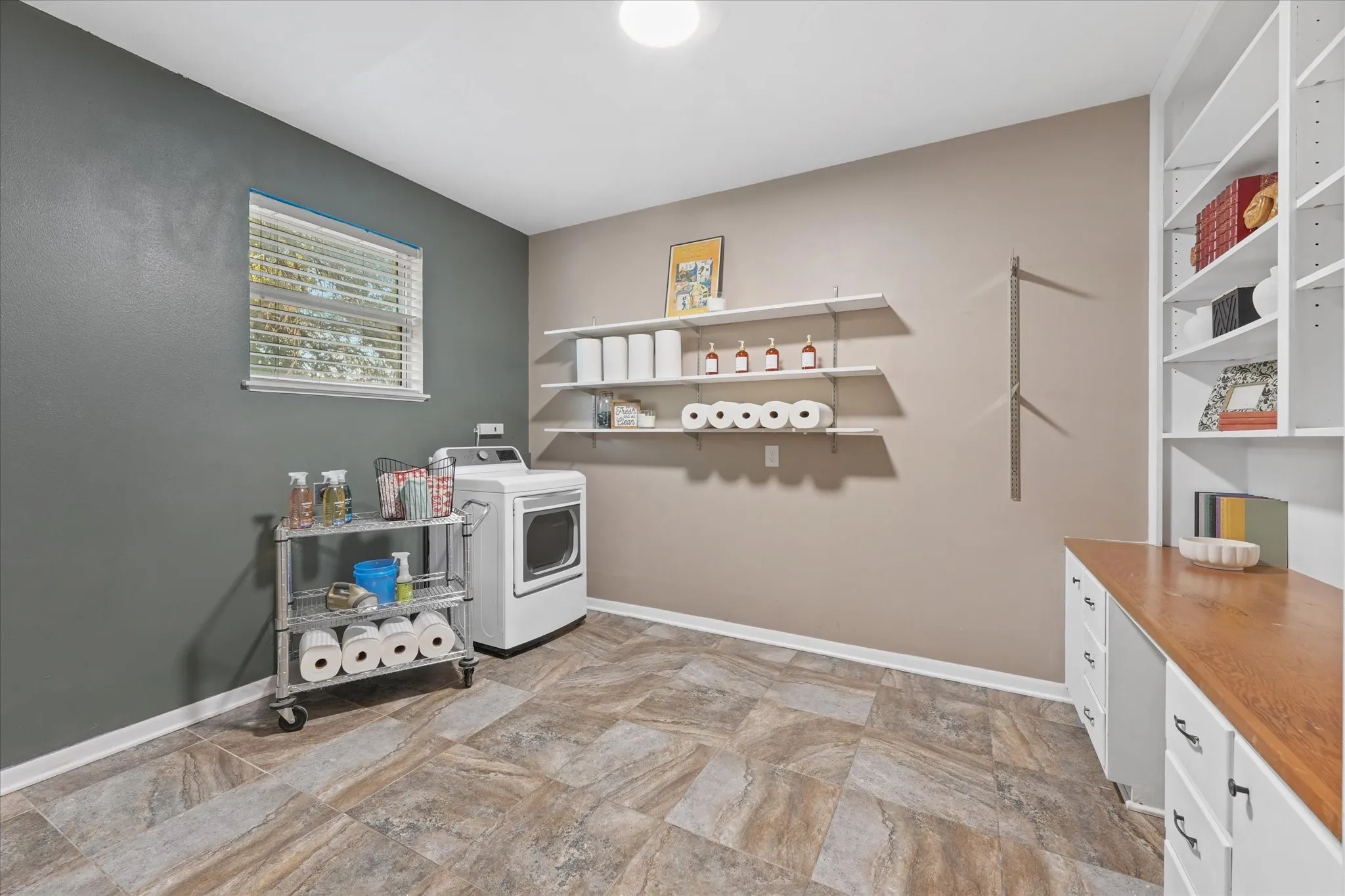 Laundry area featuring a patterned floor tile, white floating shelves, and built-in shelving with a wood-finish countertop