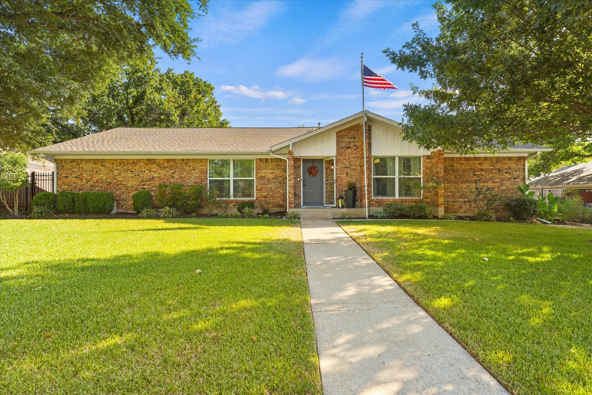 Welcome Home! Brick exterior with a gabled roofline, mature trees, and a concrete walkway