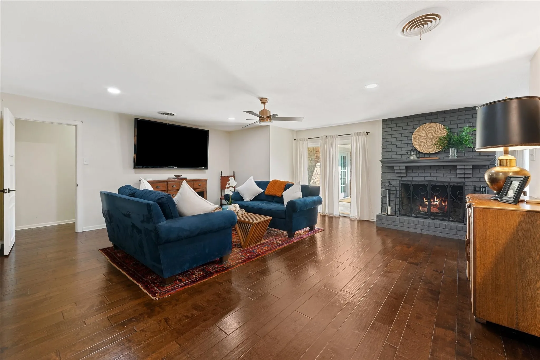 Wood-finish flooring, recessed lighting, ceiling fan, and a brick fireplace with a mantel
