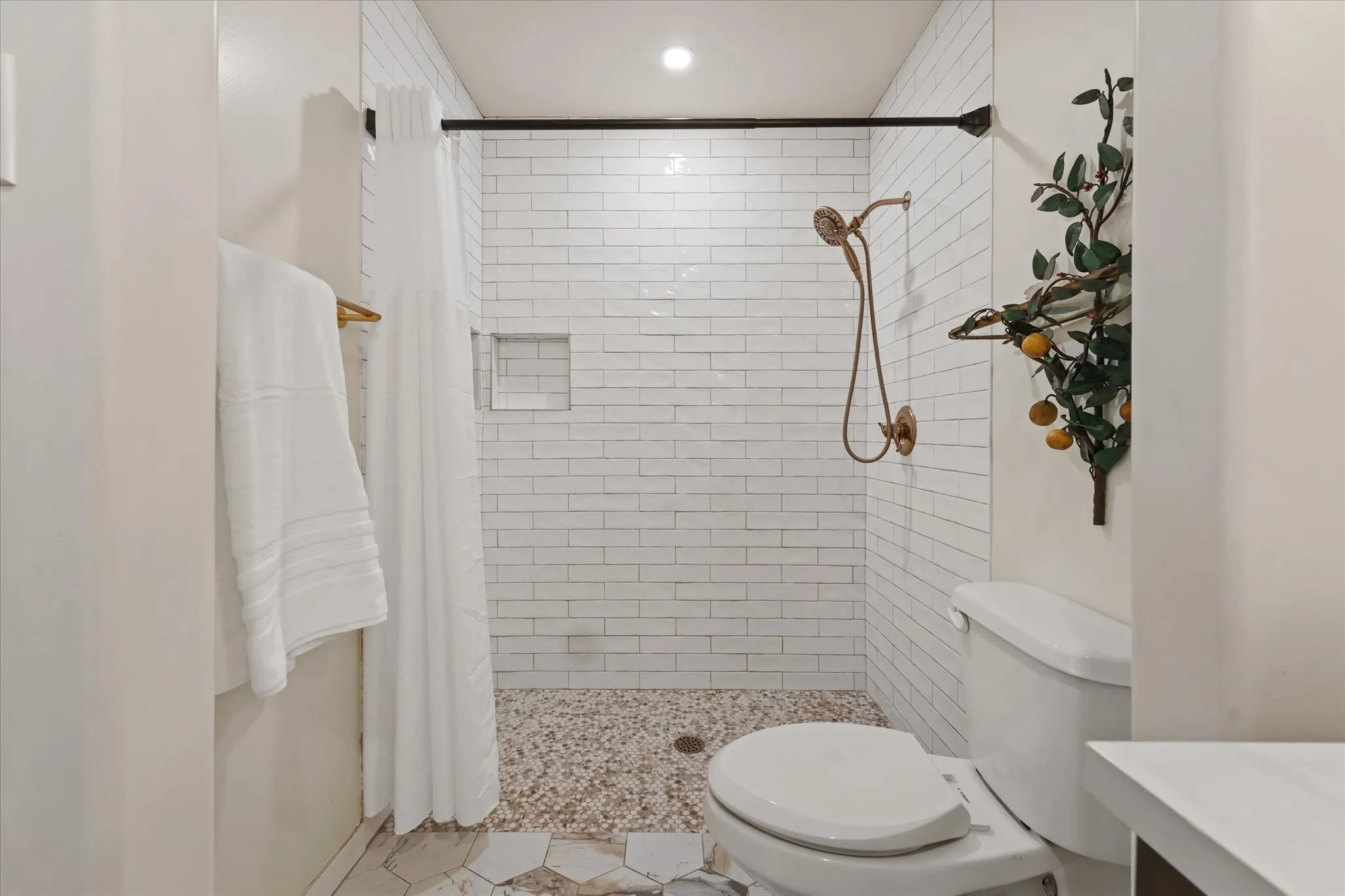 Walk-in shower with subway tile walls, pebble floor, and a built-in shower niche