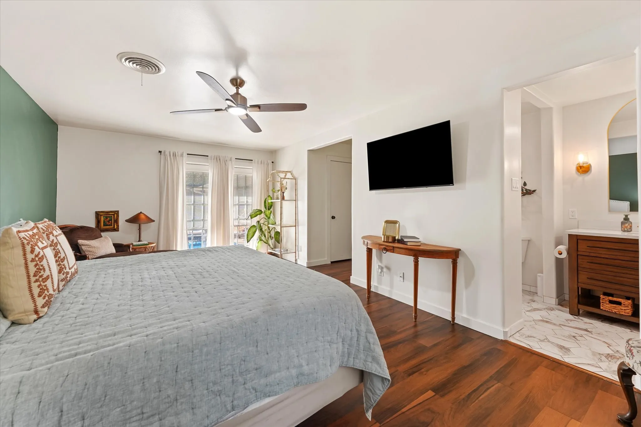 Hardwood flooring, ceiling fan, and direct access to a bathroom featuring a wood-finish vanity with a vessel sink and wall-mounted sconce