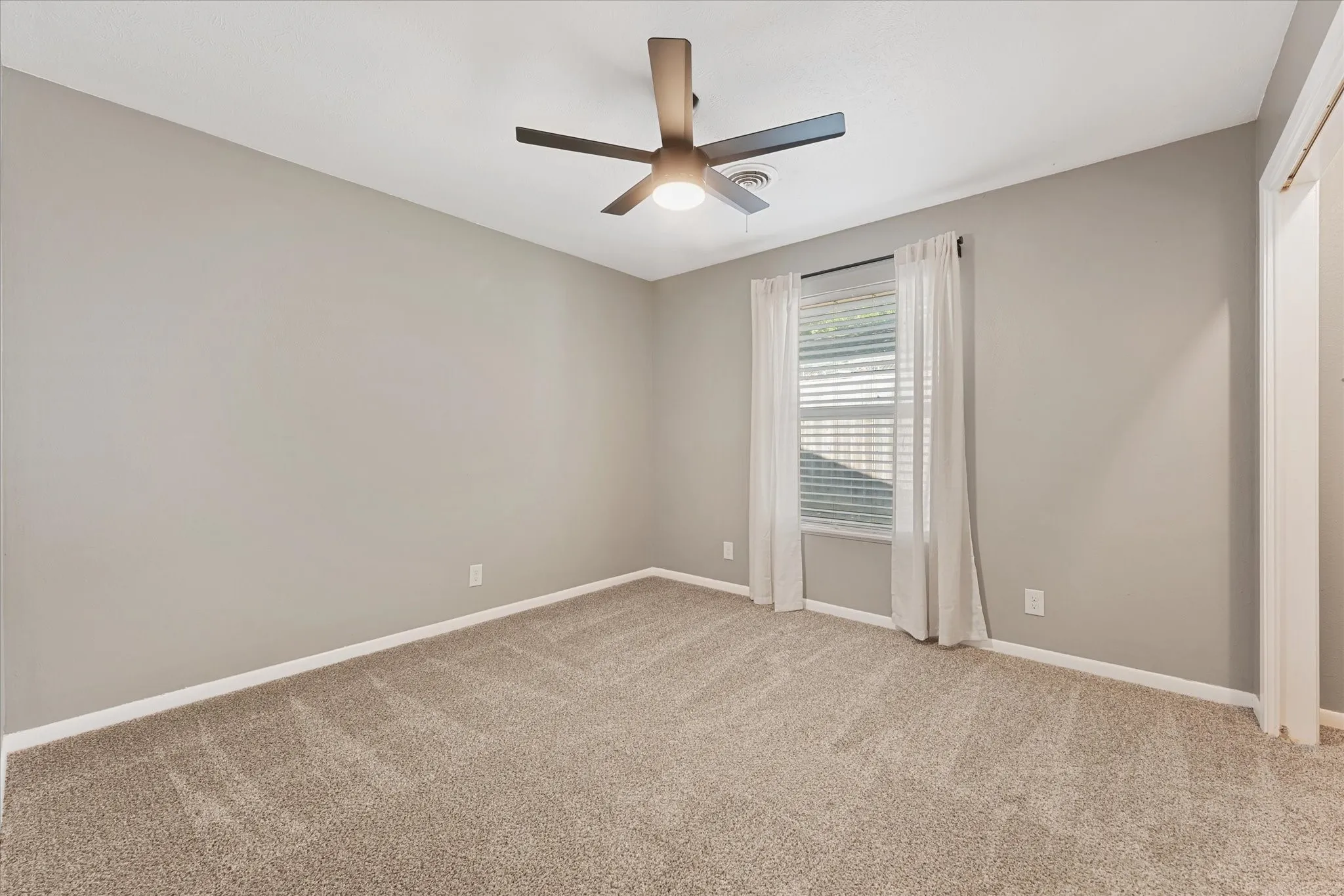 New carpeted flooring, neutral wall paint, window with blinds, ceiling fan with integrated lighting, and white trim