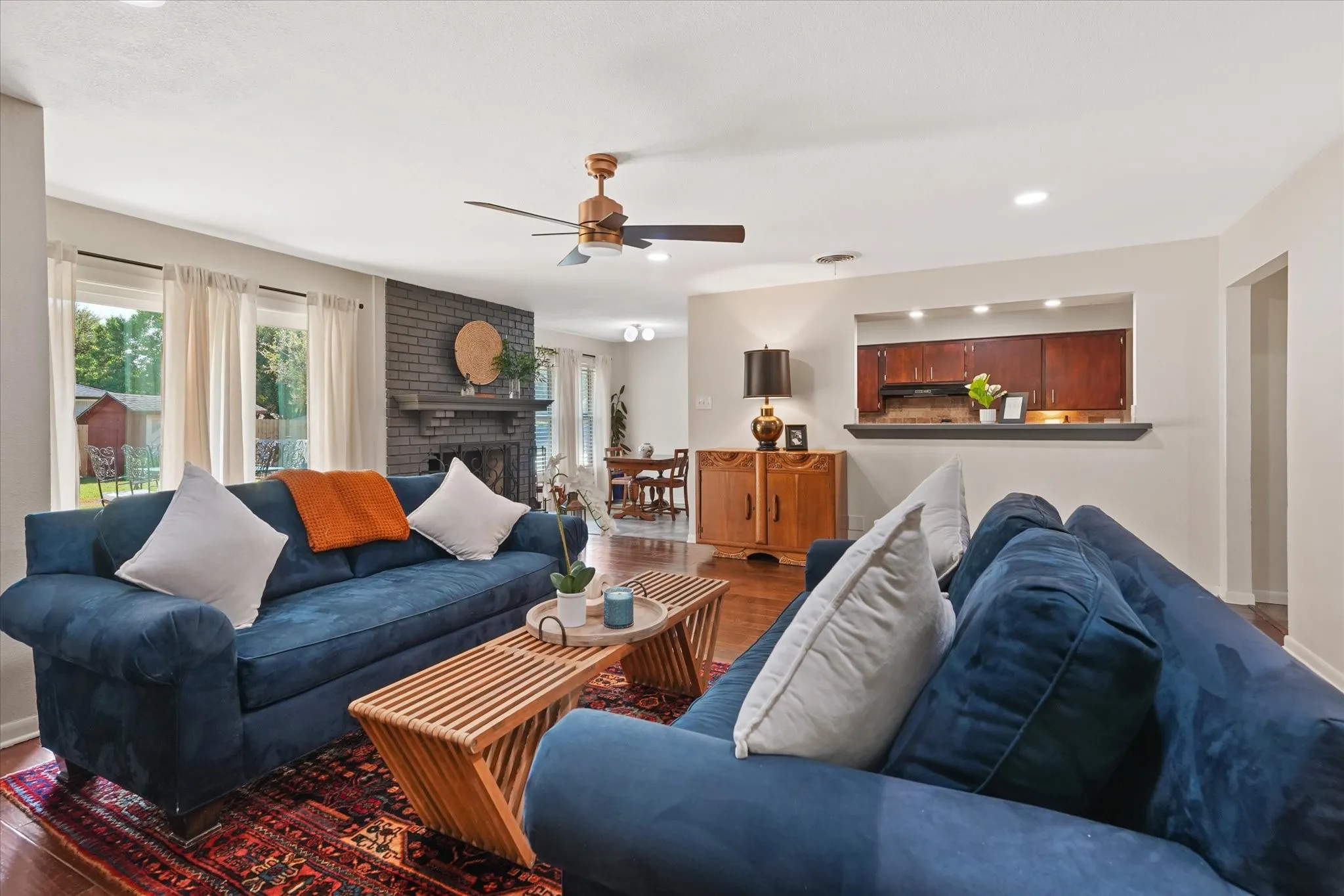 Hardwood-finish flooring, recessed lighting, brick fireplace with mantel, ceiling fan, and pass-through counter to kitchen