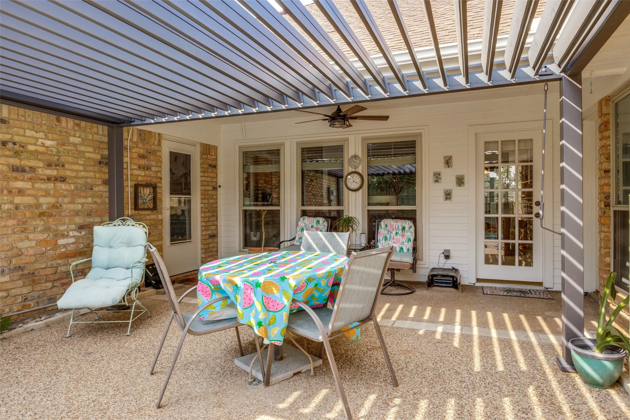 Covered patio featuring an adjustable louvered pergola, brick exterior, and exposed aggregate flooring