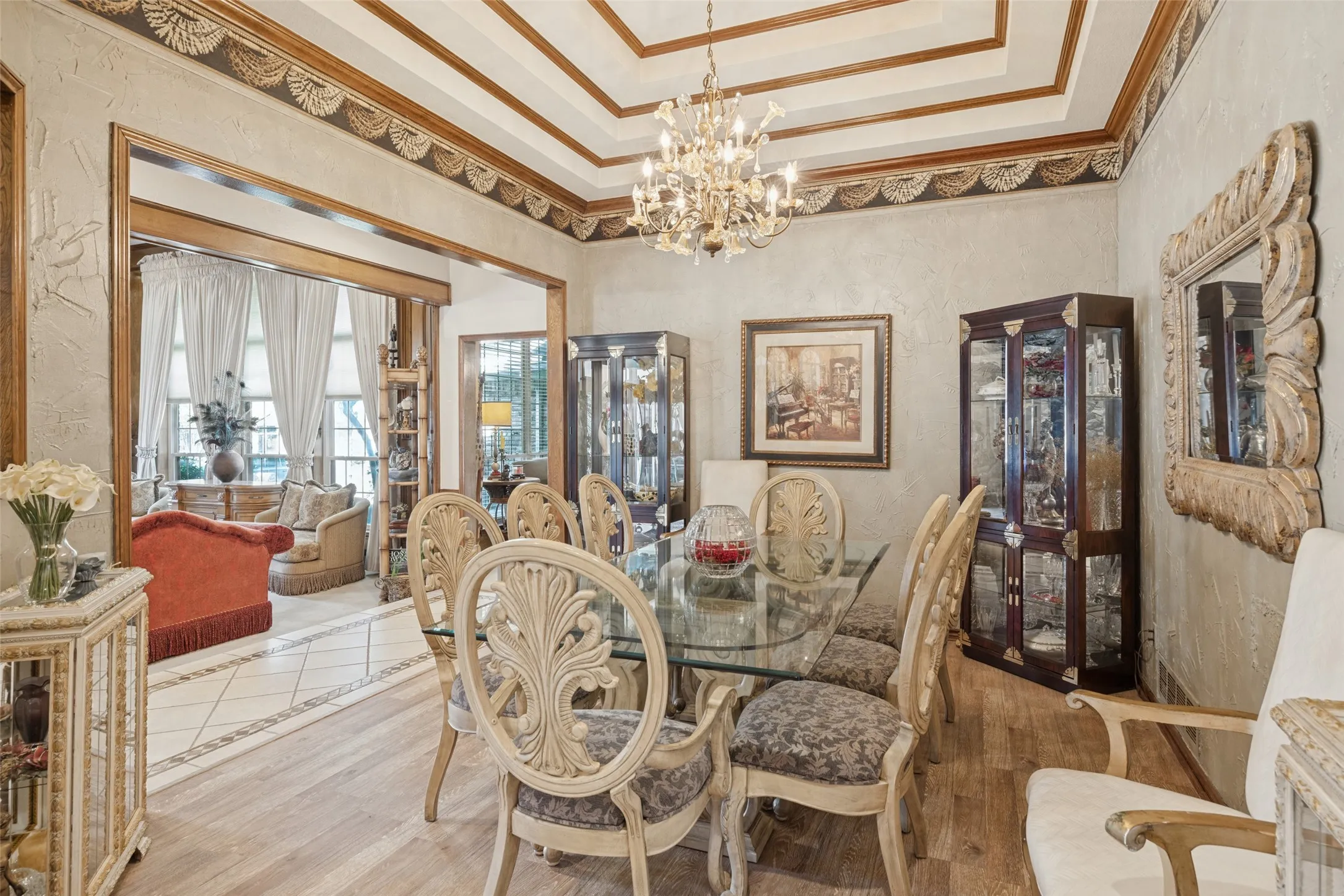 Tray ceiling with decorative wood trim, ornate chandelier, wood-finish flooring, textured wall finish, and open archway