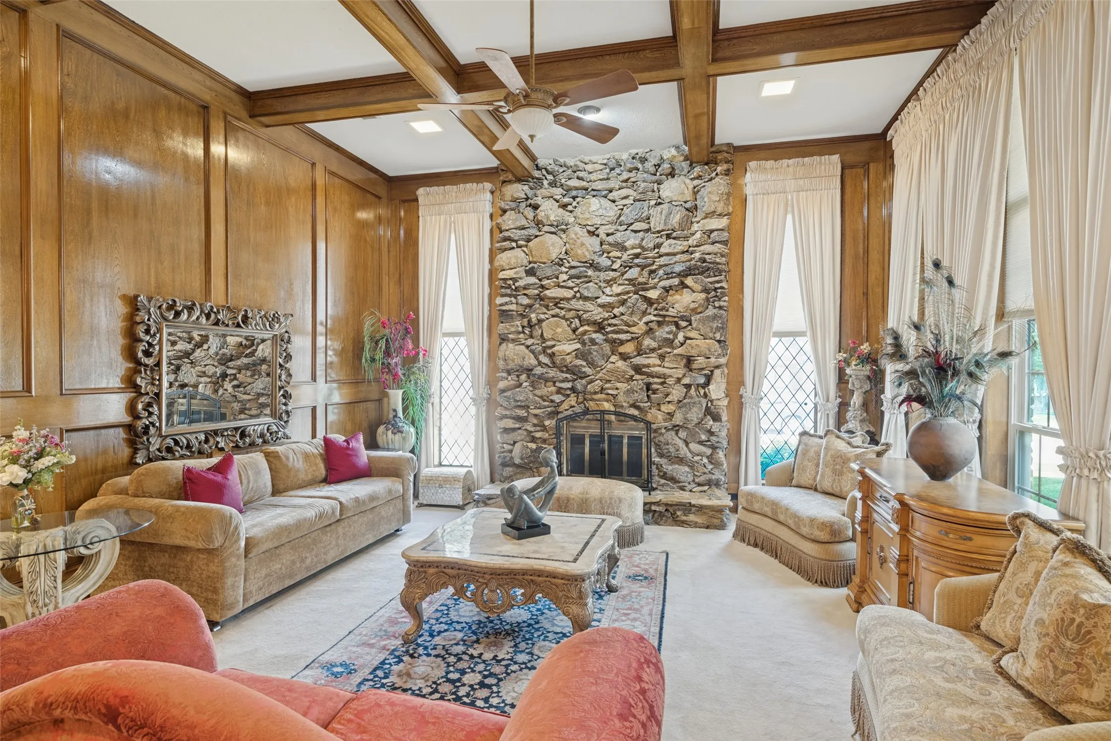 Wood-paneled walls, exposed wood beams, stone fireplace, ceiling fan