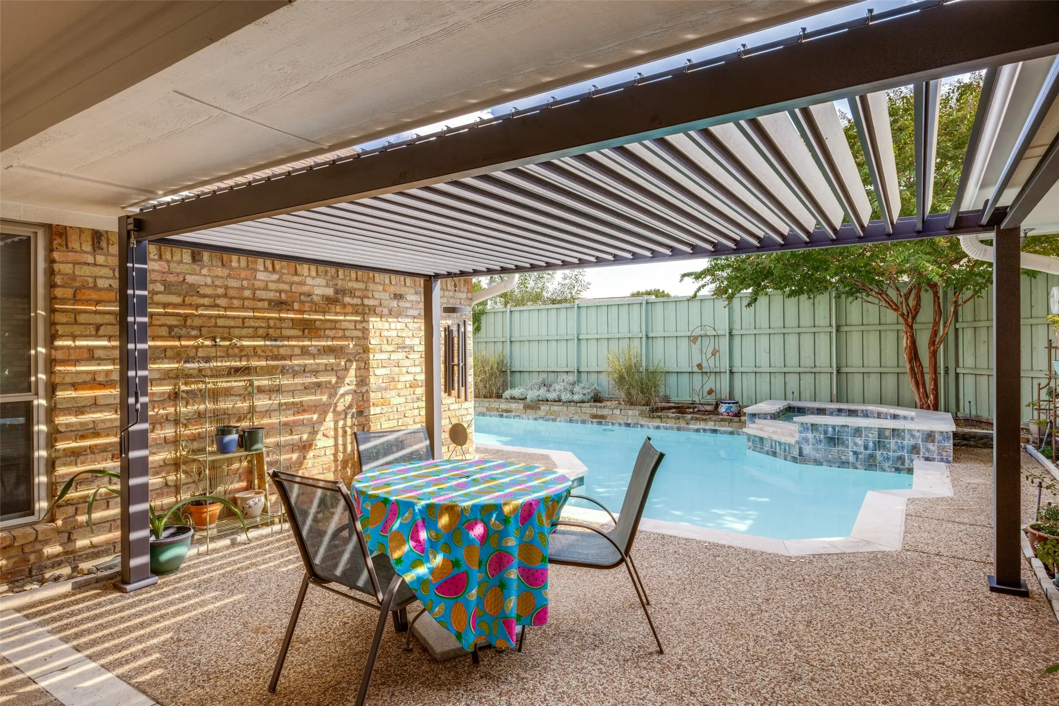 Patio with a pergola, exposed aggregate concrete, brick exterior, and a swimming pool with an integrated spa