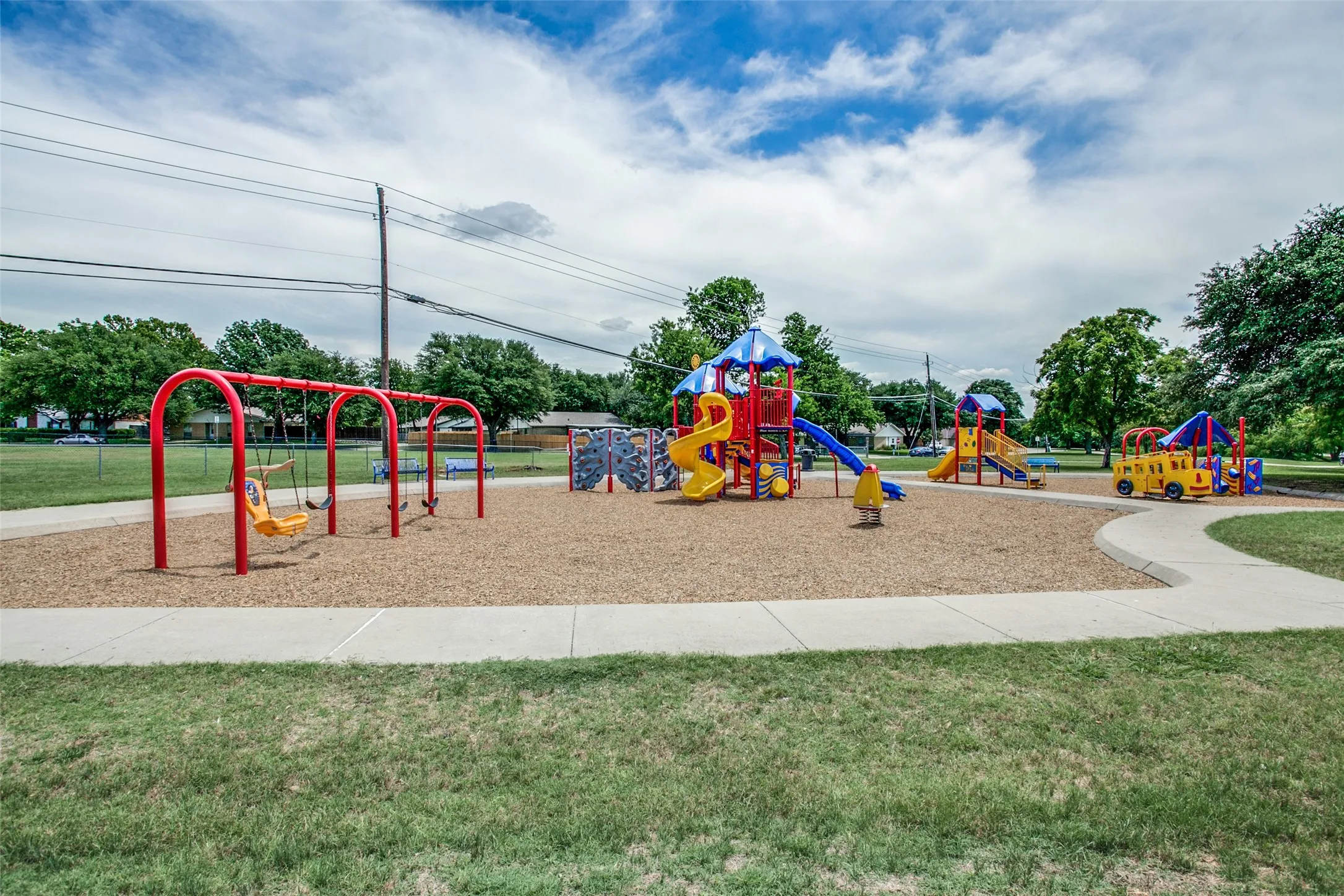 Playground area featuring multiple play structures, swings, slides, a climbing wall, and a yellow bus play feature
