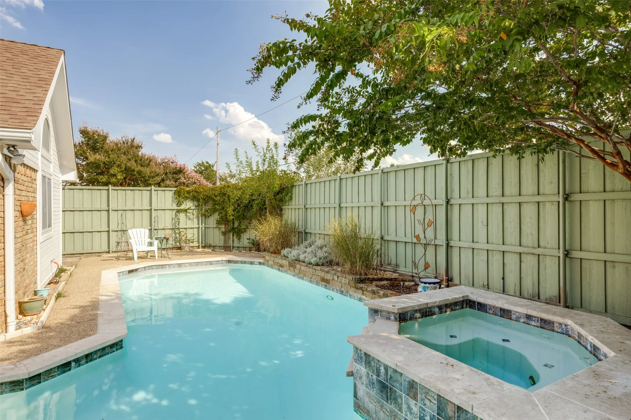 Pool and spa combination featuring tiled surrounds, complemented by a privacy fence and established trees