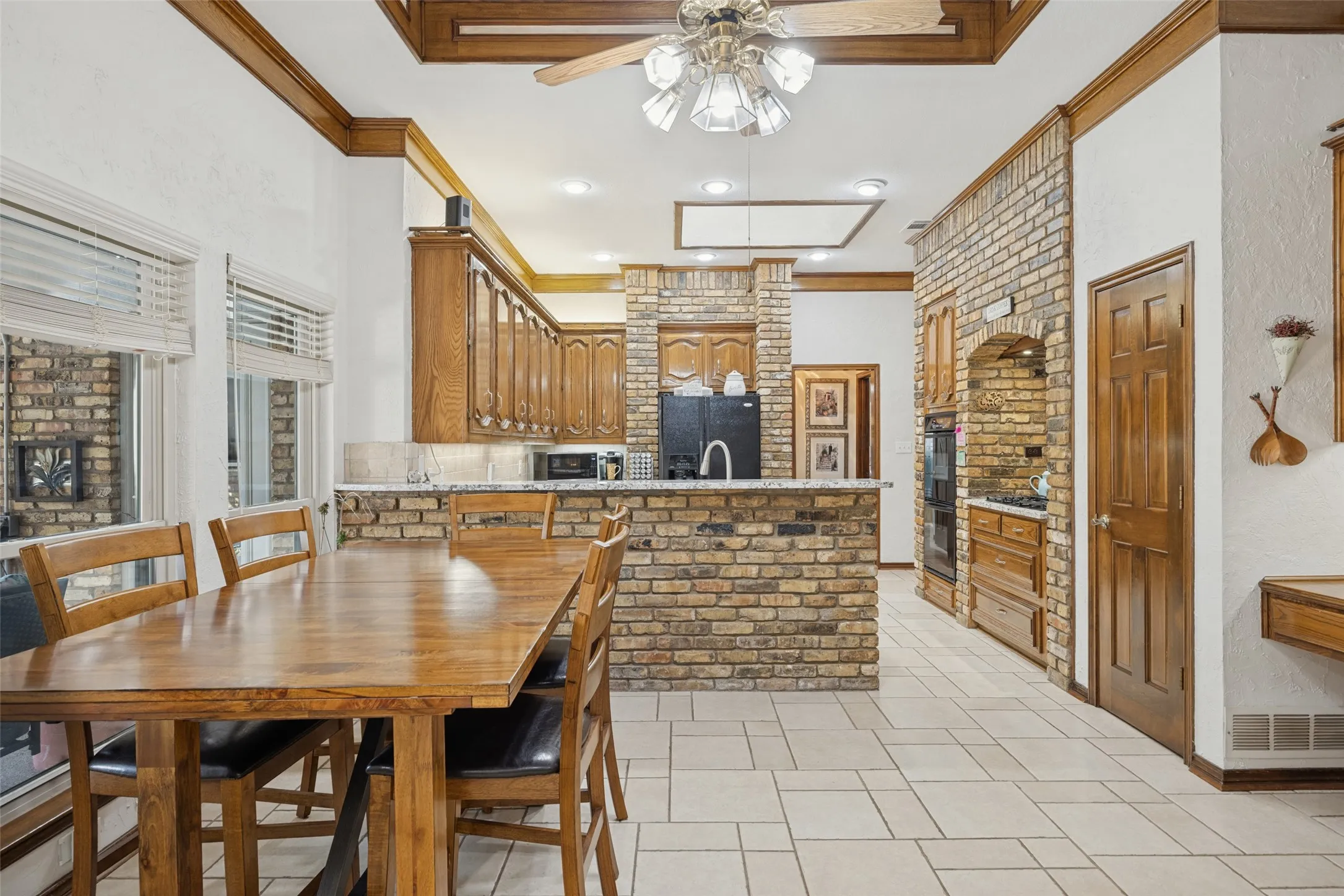 Kitchen and breakfast area featuring brick accents, wood cabinetry, and tile flooring