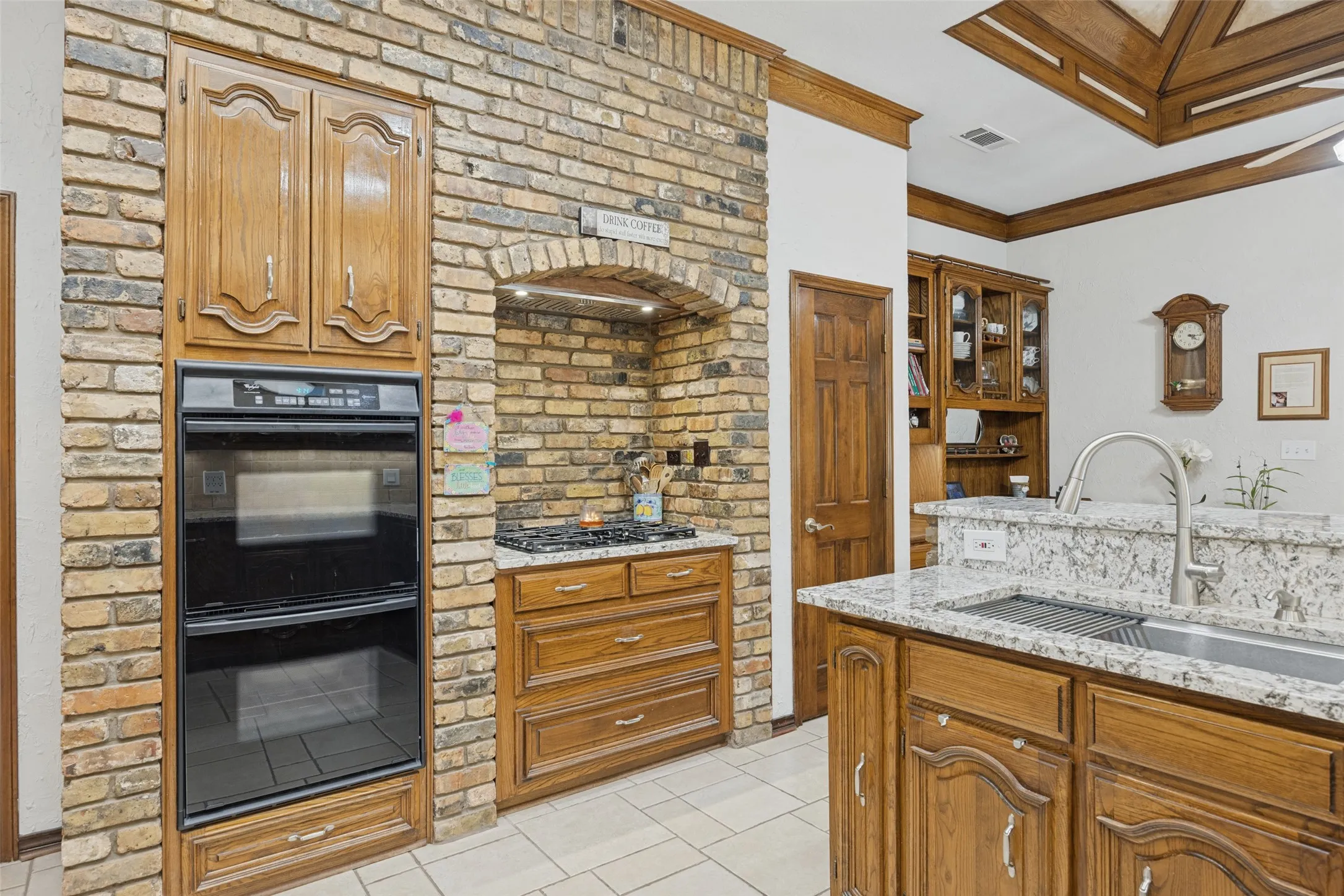 Brick-clad oven wall with integrated double oven, wood cabinetry, and a gas cooktop