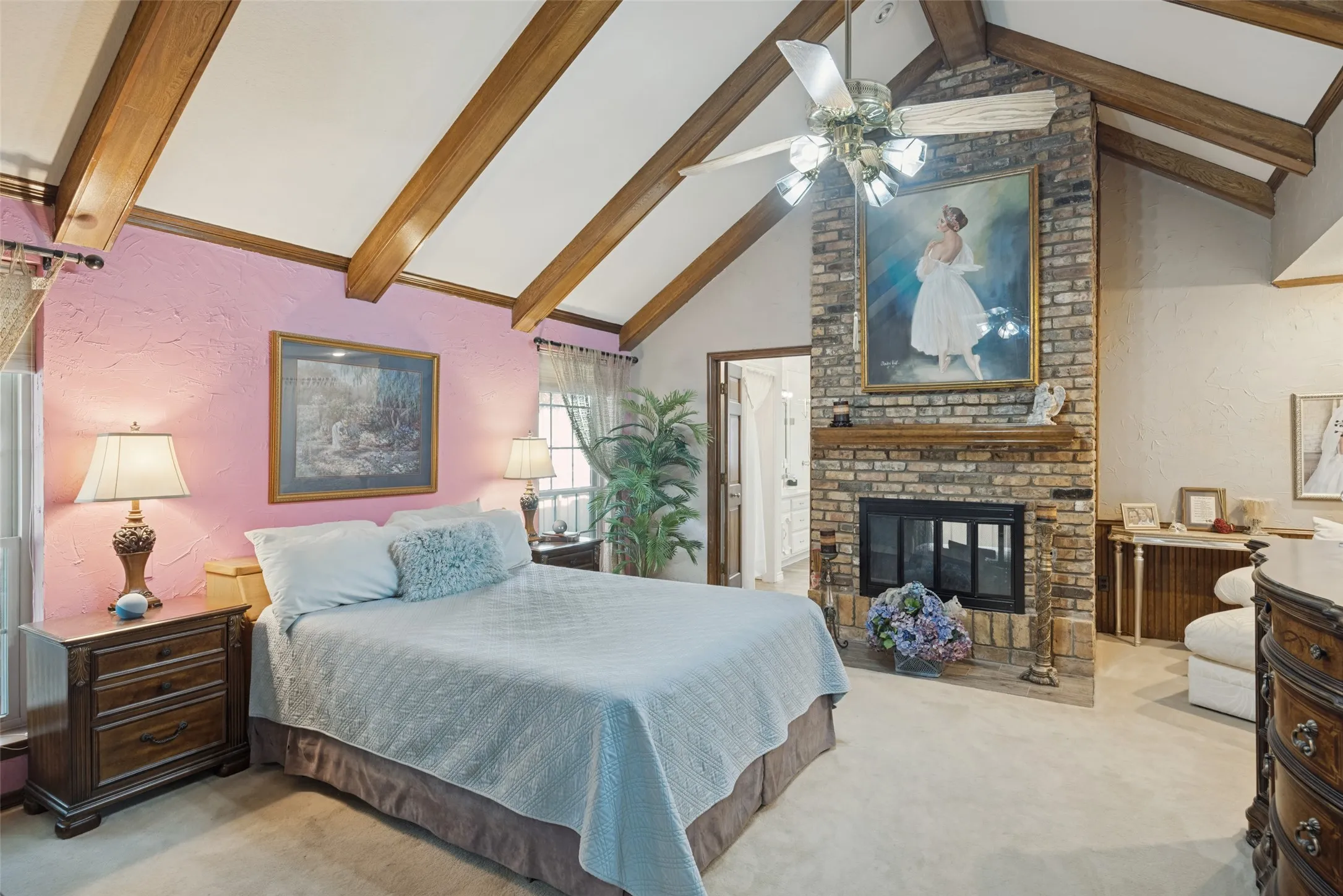 Vaulted ceiling with wood beams, brick fireplace with mantel, ceiling fan, and carpeted flooring