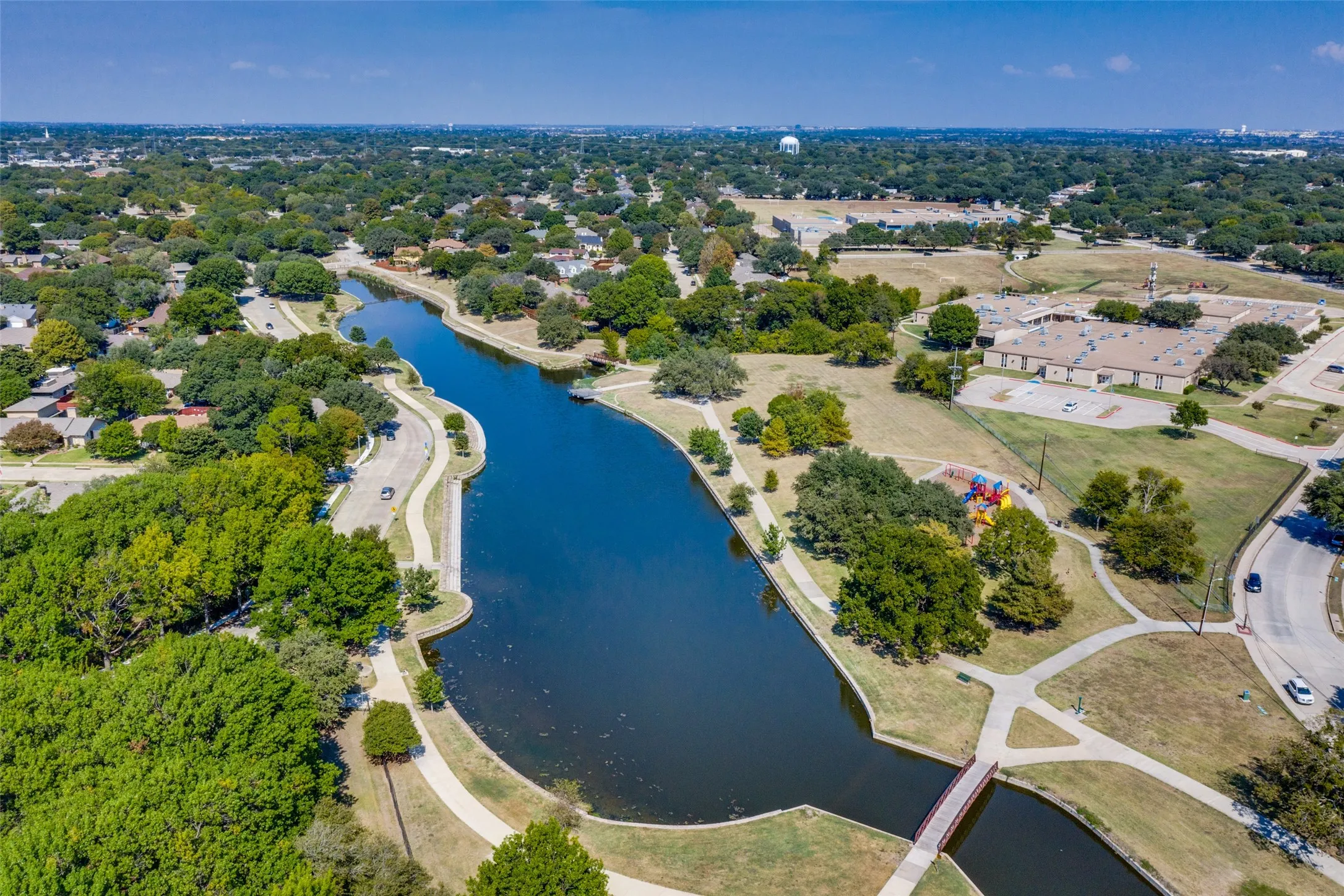 Waterfront setting with winding pedestrian paths, mature trees, and a nearby recreational area