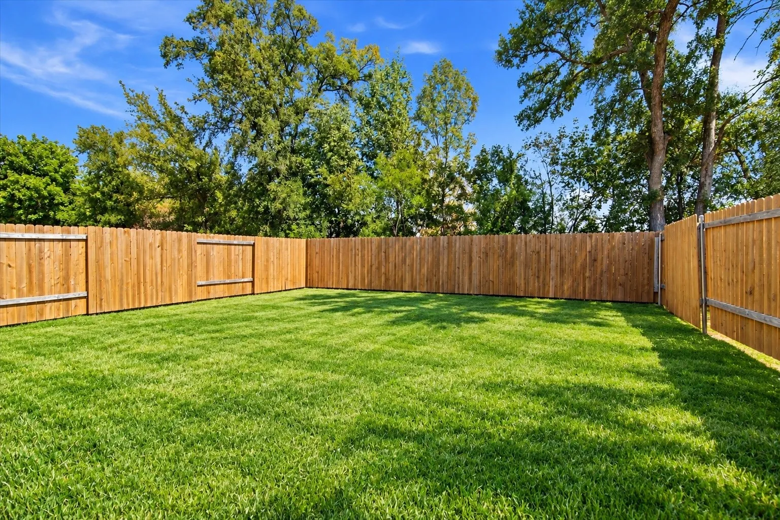 Expansive backyard with a manicured lawn, fully enclosed by a wood privacy fence, featuring mature perimeter trees