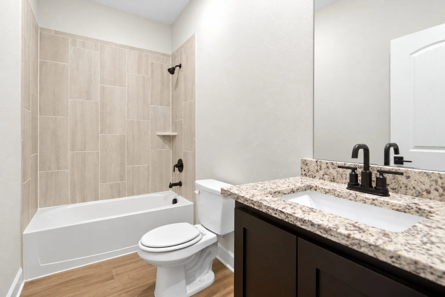 Bathroom featuring a built-in tub with full tile surround, dark wood-finish vanity with an undermount sink, and a speckled countertop