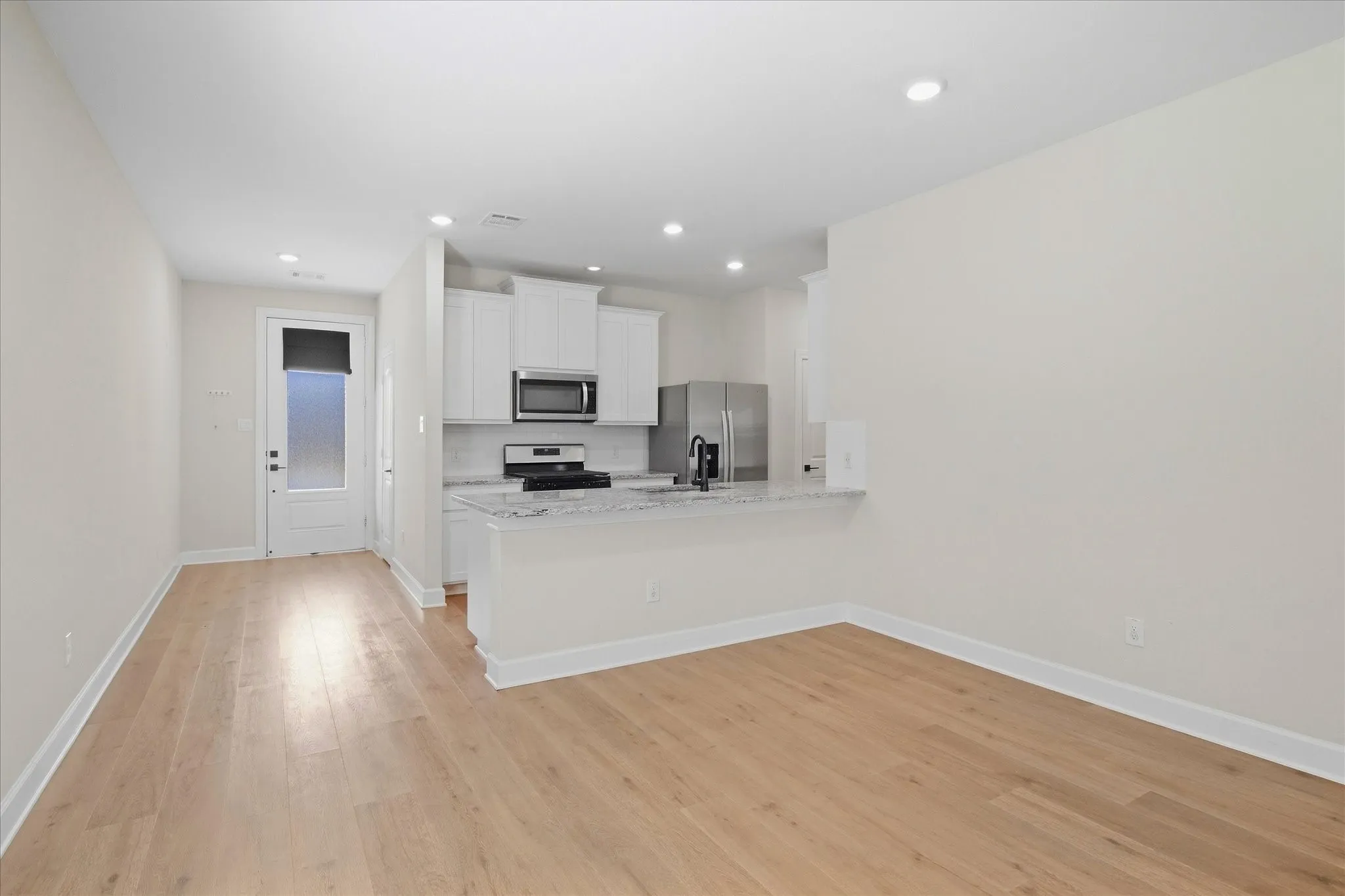 Wood-finish flooring, recessed lighting, white cabinetry, integrated stainless steel appliances, and a breakfast bar with stone countertops