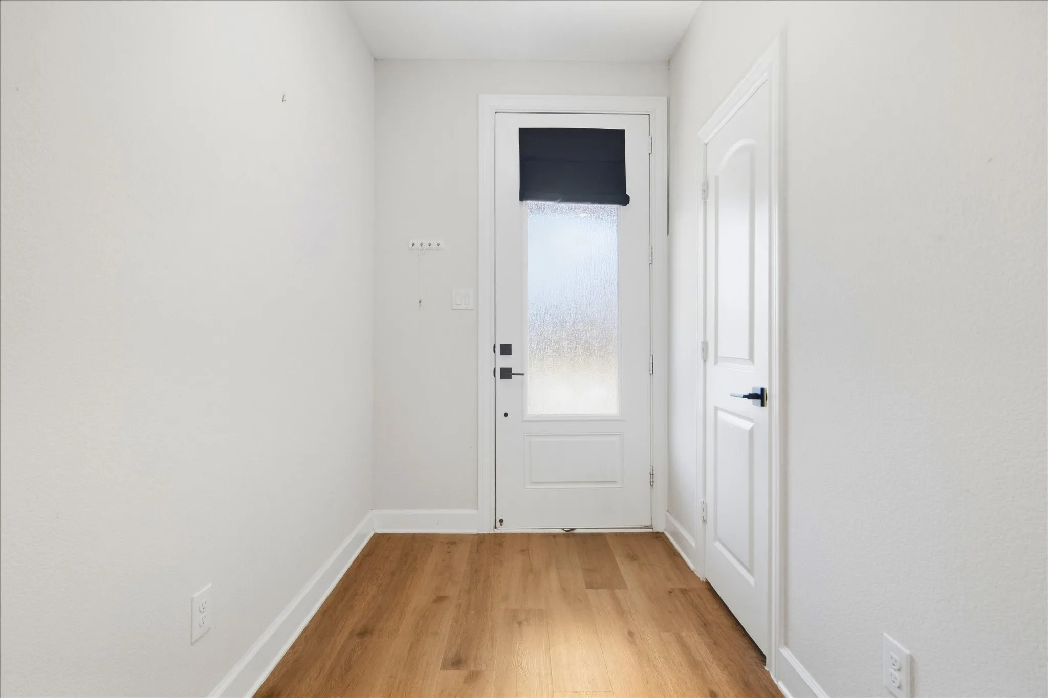Wood-finish flooring, white walls, and a white door with a frosted glass panel