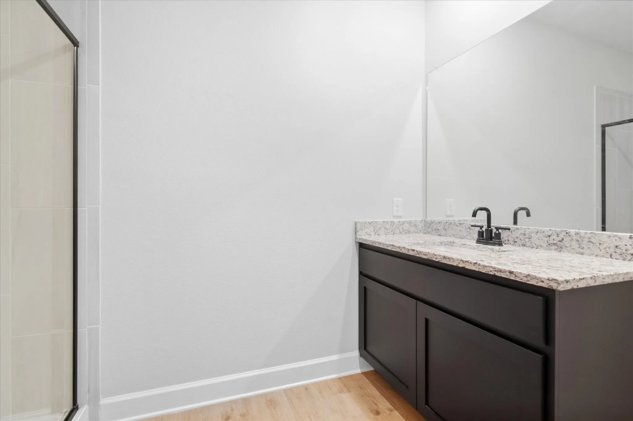 Dark wood-finish vanity with a light granite countertop, undermount sink, and black faucet