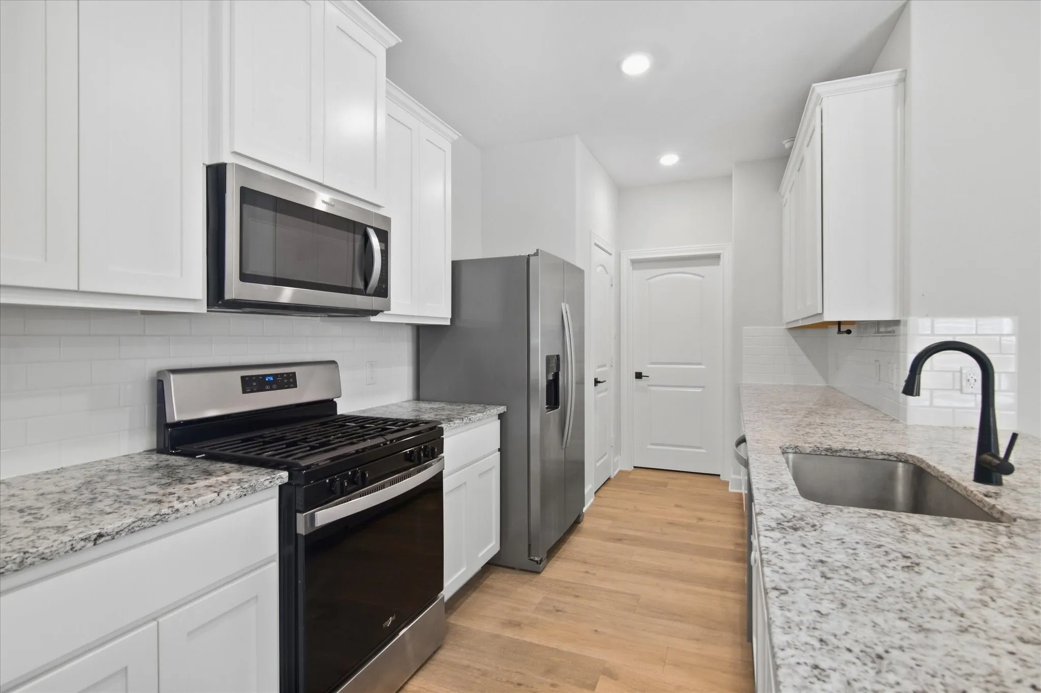 White cabinetry, stainless steel appliances, granite countertops, subway tile backsplash, and wood-finish flooring
